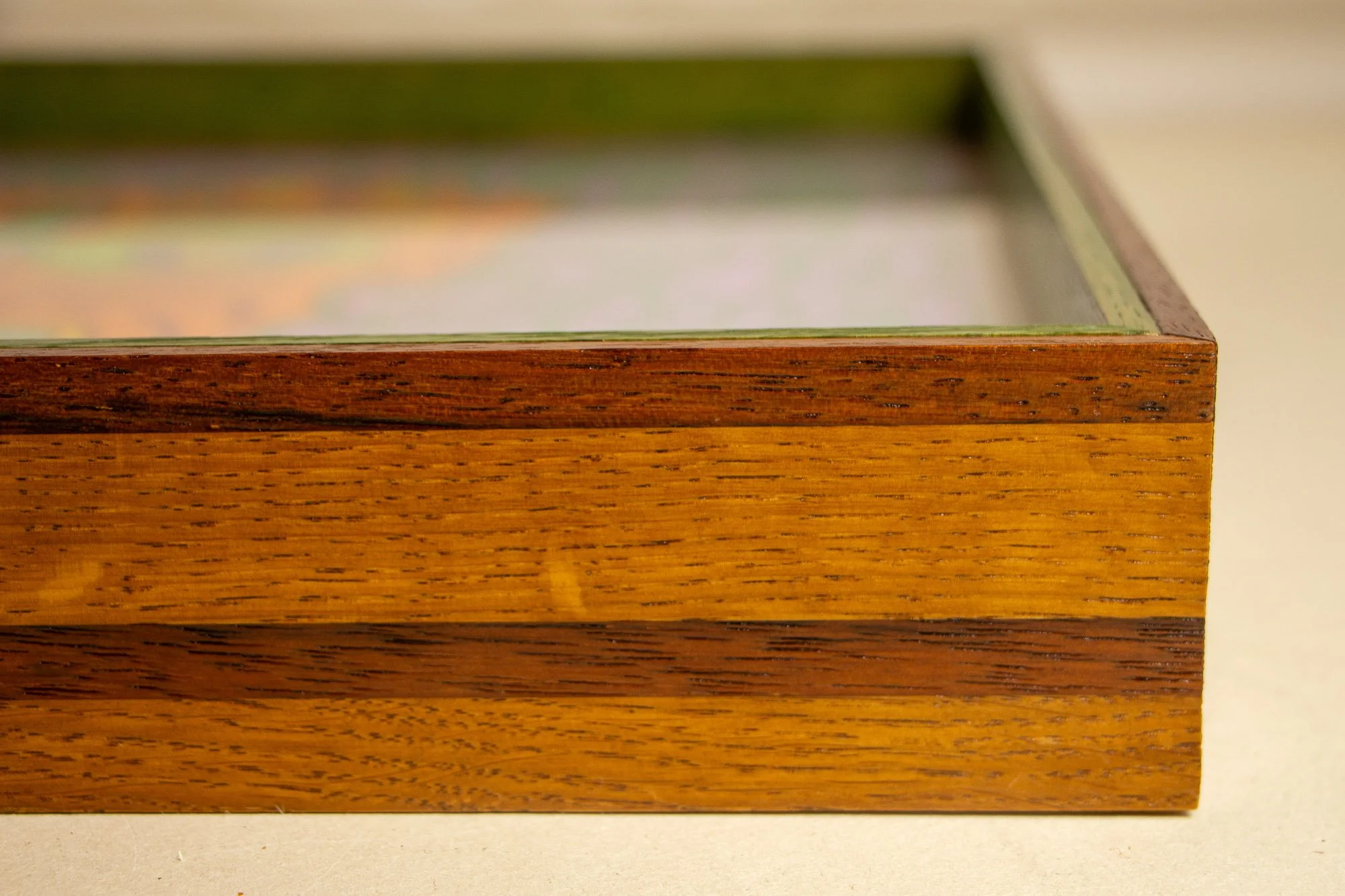 Unseen Signifiers 002 frame detail: angled corner view of the frame, showing the glass edge, the clean miter join, and the green-toned inner lip set against the warm brown outer profile. mahogany, oak and beech wood.