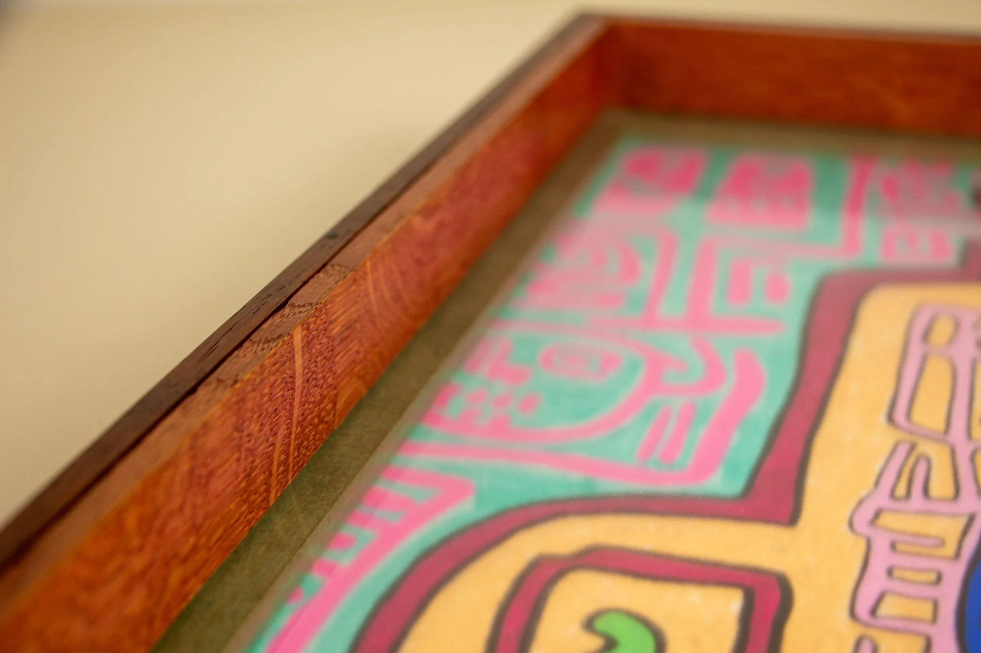 Unseen Signifiers 004 frame detail: oblique top-edge detail showing the reddish-brown outer rail, olive-green inner reveal, and the artwork’s pink symbolic forms visible beneath the glass. mahogany, oak and beech wood.