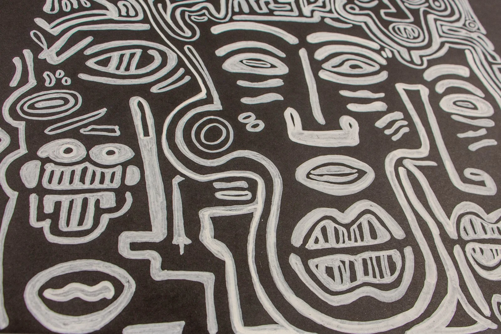 Metamorphic Entwining 003 detail: trio of faces, left totem with barred teeth and tongue, center face with spiral ear and stacked lips; white ink on black paper