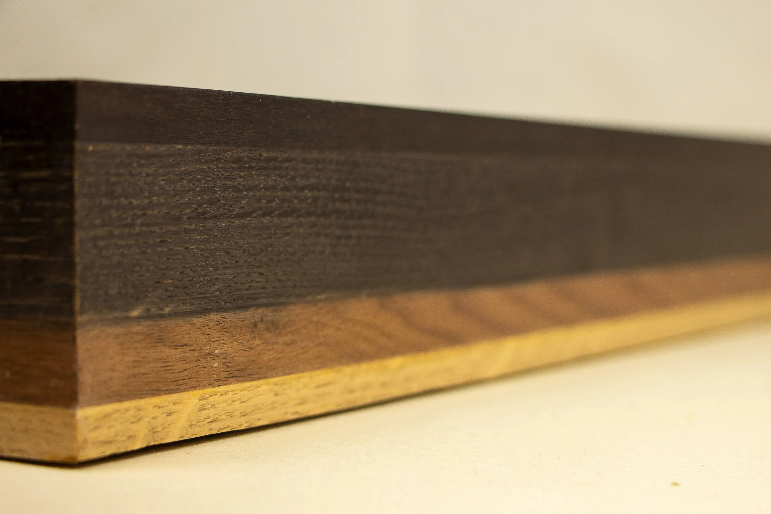 Mêlée of Discovery 004 frame: angled exterior detail showing the frame depth and the gradual tonal shift across the stacked walnut and oak bands.