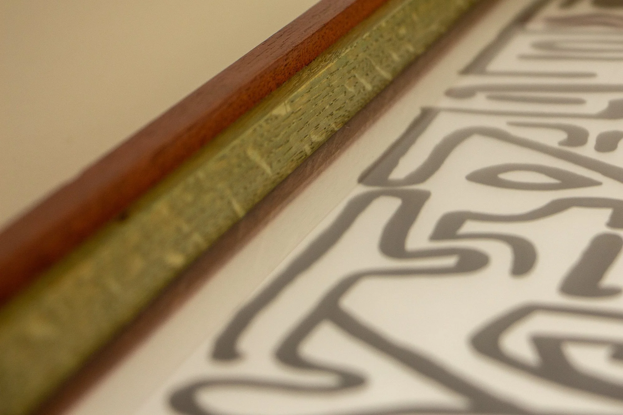 Resonant Syntax 001 frame: angled close-up of the inner oak spacer and outer mahogany band, showing the triadic color rhythm and the artwork surface below the glass