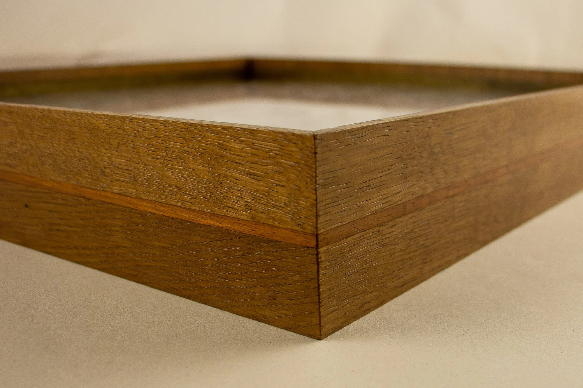 Veiled Alchemist 002 frame detail: corner close-up of the outer frame, highlighting the precise mitre, the layered wood construction, and the fine red-toned band set between the warm elm sections.