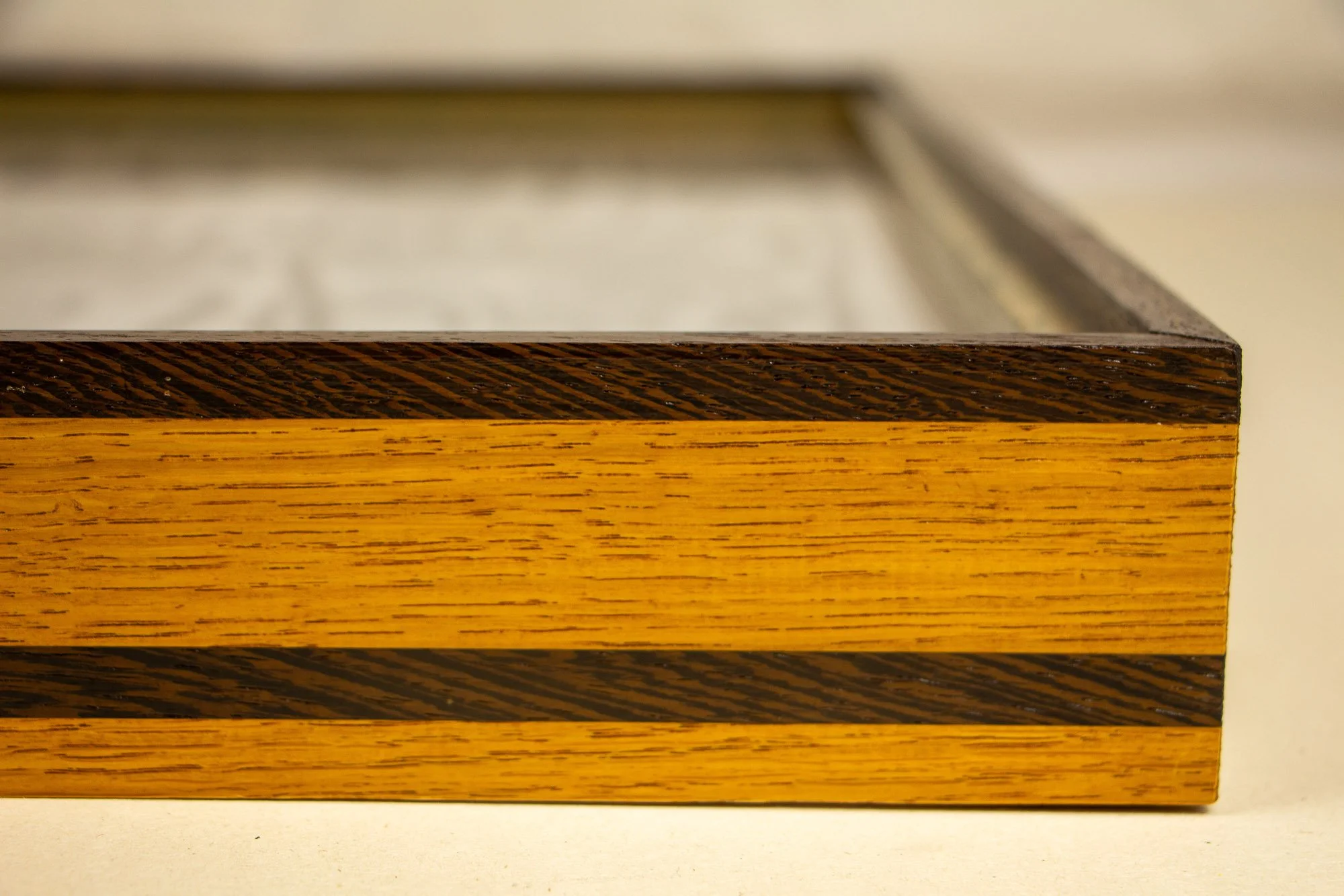 Elusive Cocoon 004 frame: frontal side detail of the layered wengé-and-oak frame, showing a bright yellow-toned oak band, dark wengé rails, visible grain, and a shallow low-profile construction.