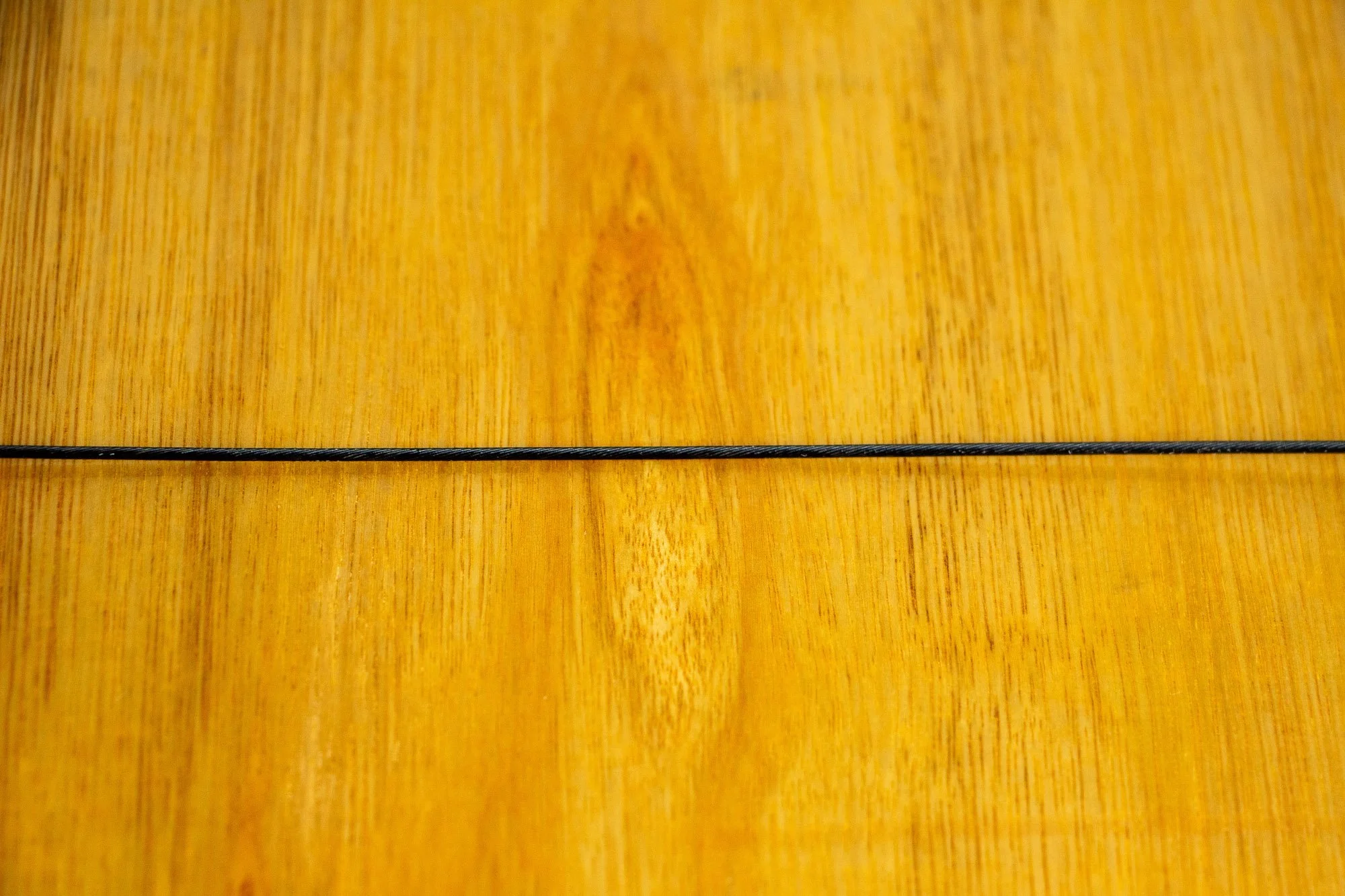 Unseen Signifiers 004 frame detail: back-panel detail with the black hanging wire running horizontally across the warm plywood surface, emphasizing the clean finish and subtle wood grain.