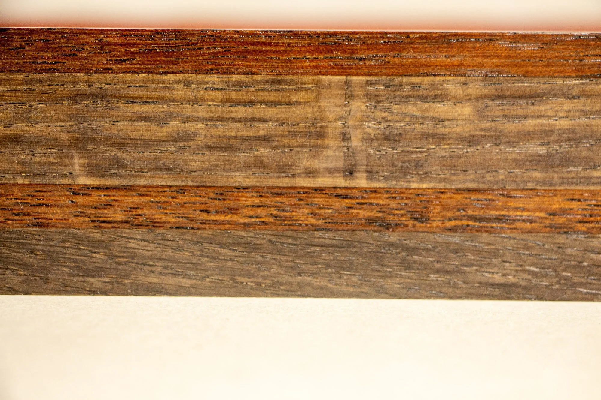 Unseen Signifiers 003 frame detail: frontal close-up of the frame profile, emphasizing the alternating dark and warm wood tones and the long horizontal rhythm of its layered construction. mahogany, oak and beech wood.