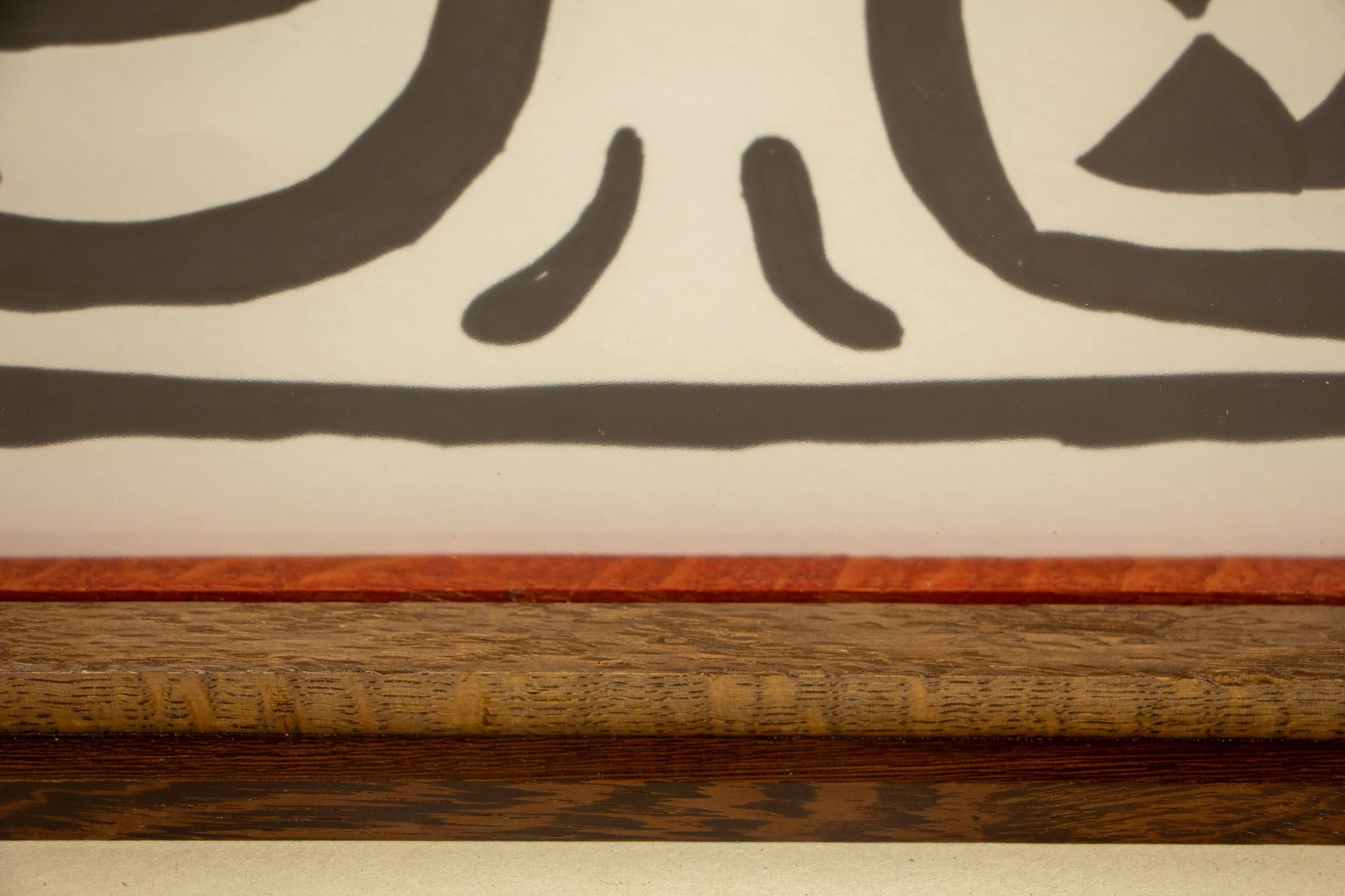 Elusive Cocoon 001 frame: upper edge detail with dark palisander outer rail, light ash-toned band, and a narrow red inner liner bordering the black ink drawing beneath the glass.