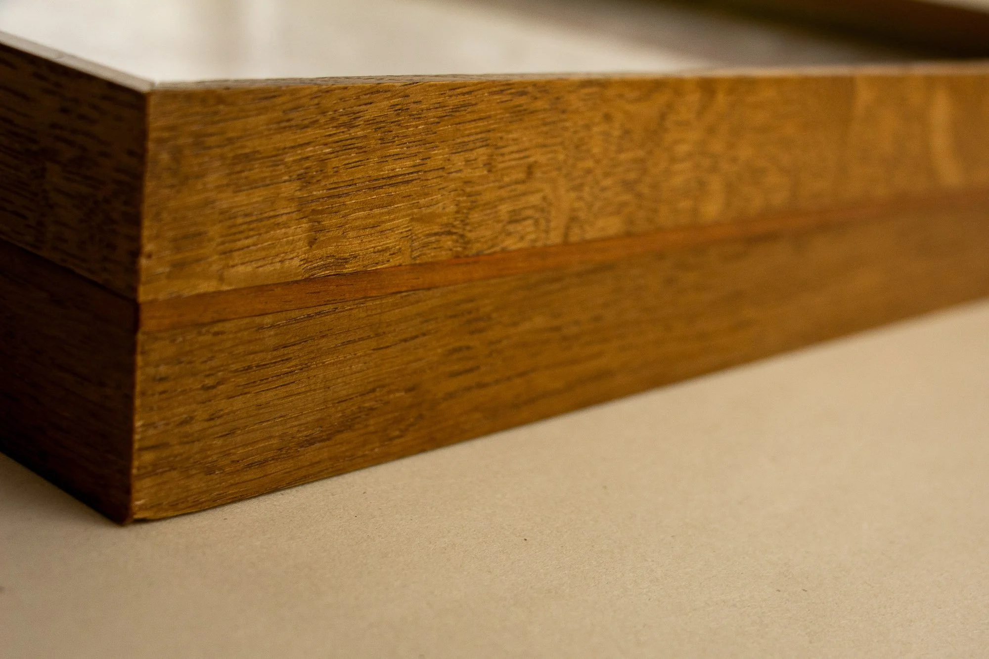 Veiled Alchemist 002 frame detail: long angled view across the front edge of the frame, emphasizing the quiet grain of the wood, the narrow inner band, and the restrained depth of the profile.