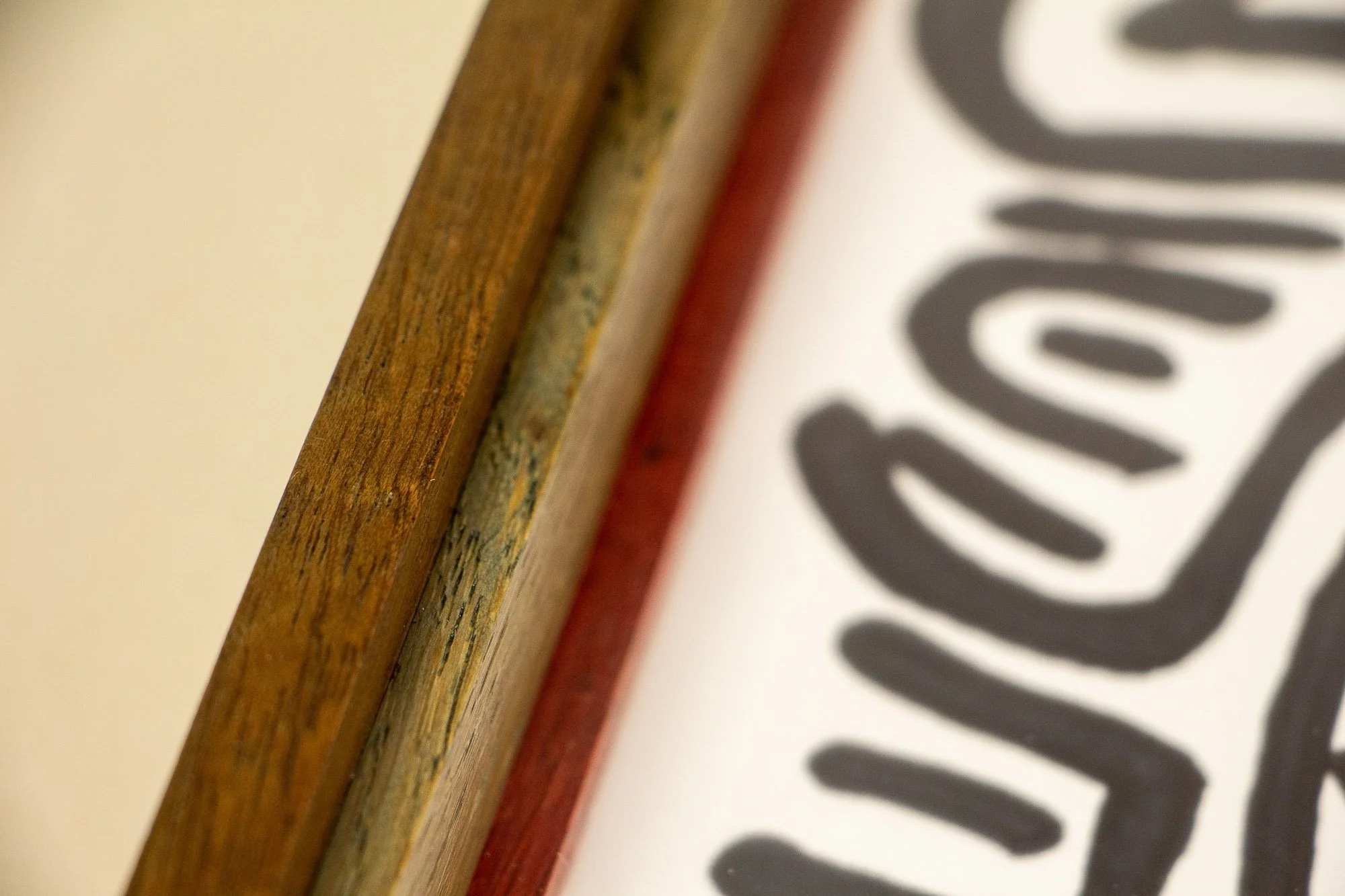 Resonant Syntax 002 frame: angled close-up of the frame edge, highlighting the layered oak and mahogany construction, the shifting color rhythm, and the artwork surface below