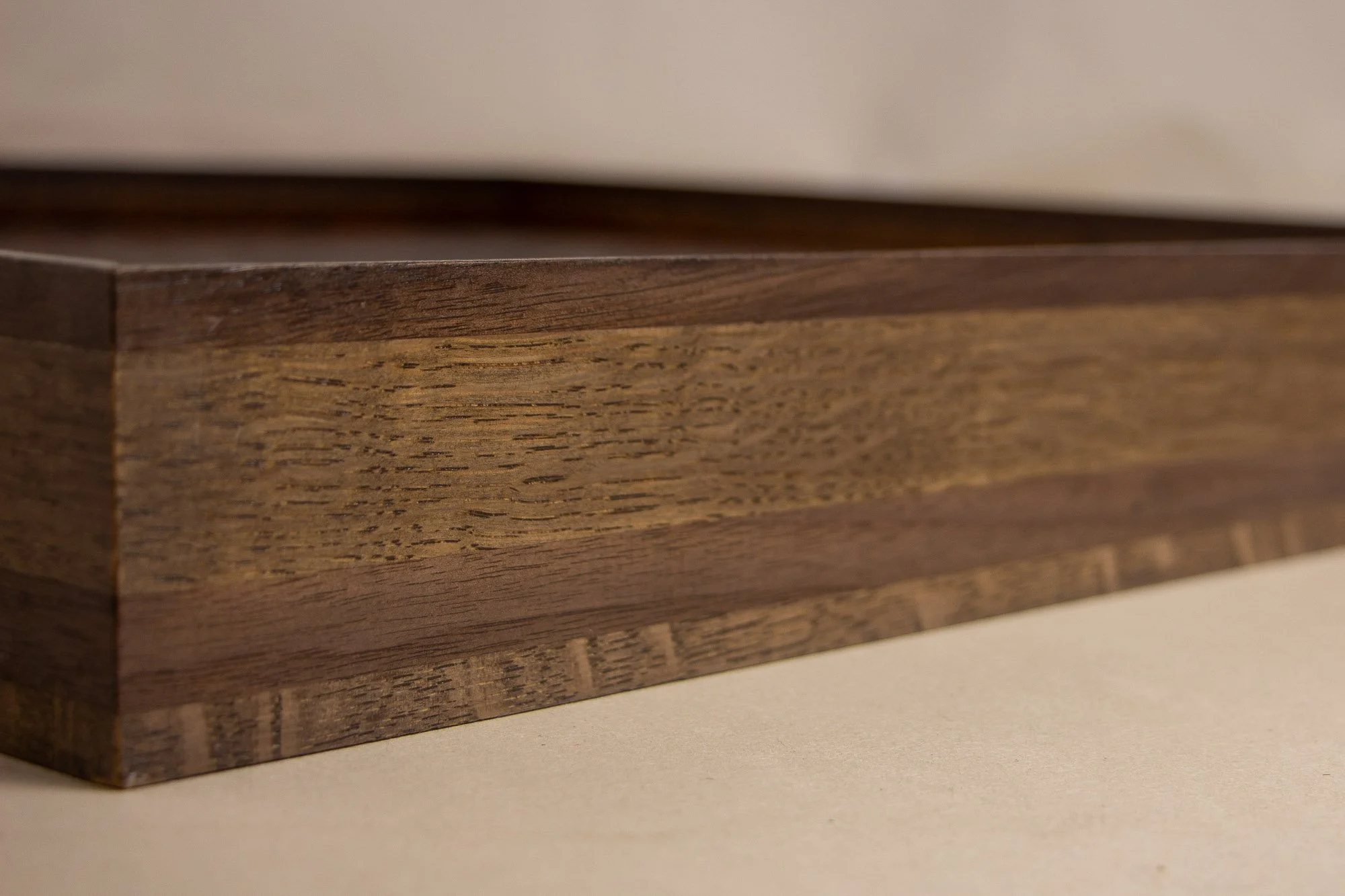 Luminous Parallax 001 frame: close-up along the upper inner edge of the frame, where the dark outer band meets a warm, vividly grained inner wood layer, seen through the shallow blur of the glazing.