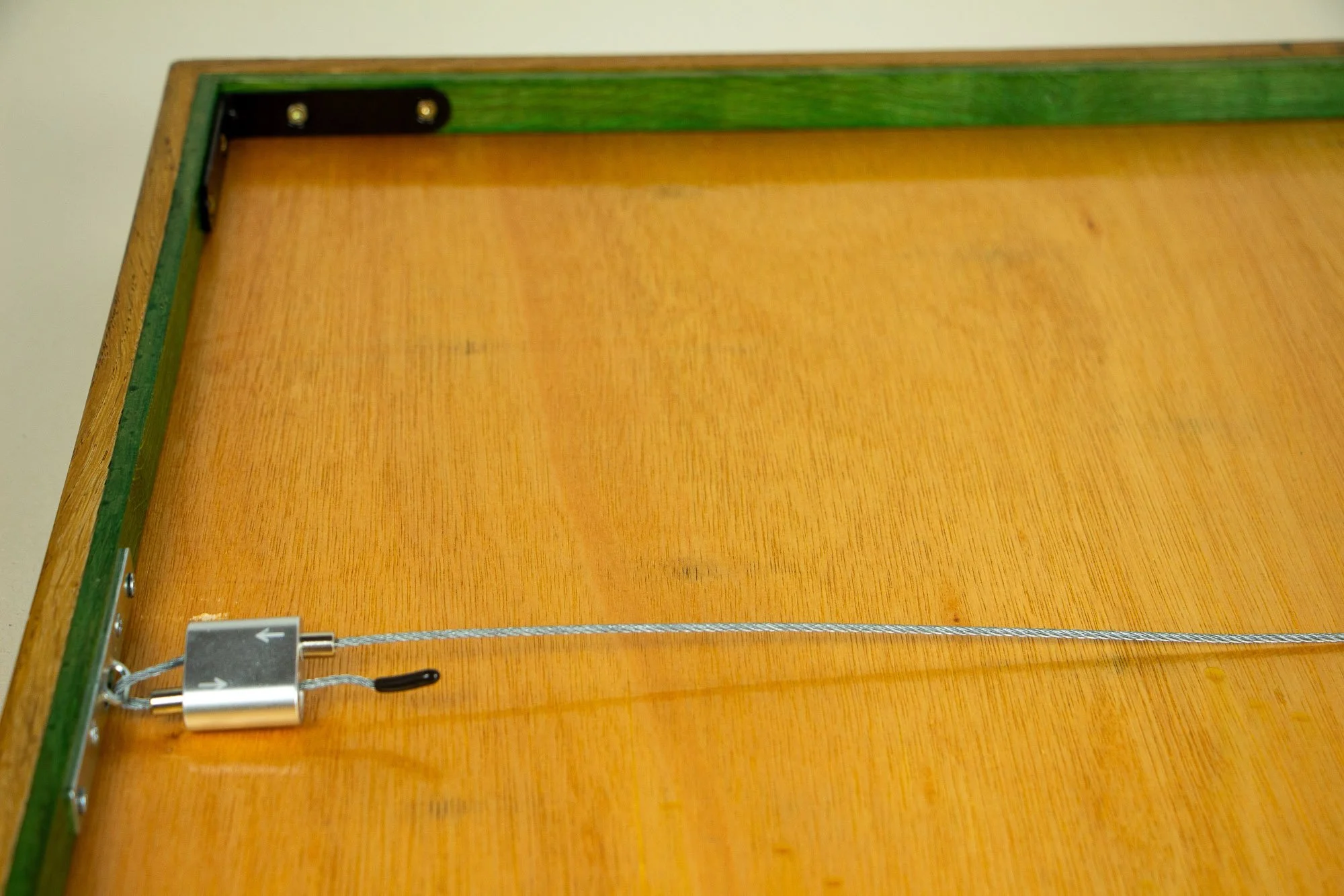 Elusive Cocoon 004 frame: reverse-side view with meranti plywood back panel, green-toned inner rim, and suspended steel hanging wire fixed across the back of the frame.