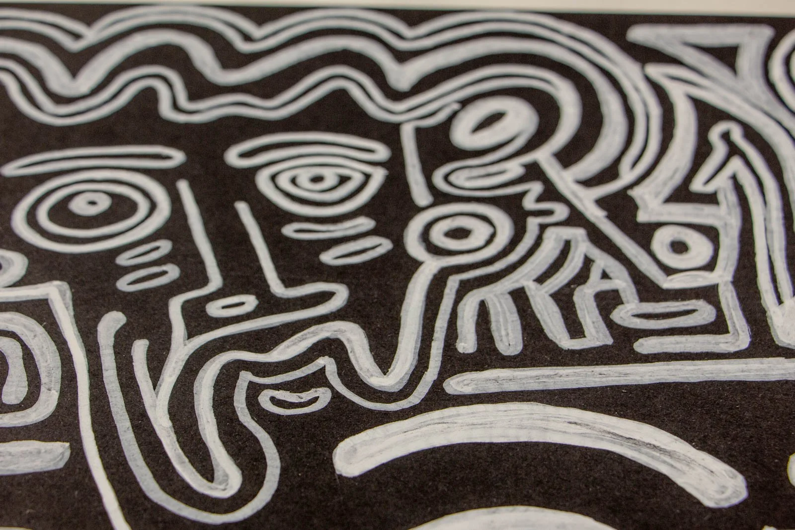 Metamorphic Entwining 003 detail: wavy-haired head with concentric eyes, curled moustache line and beard-like strokes; white ink on black paper