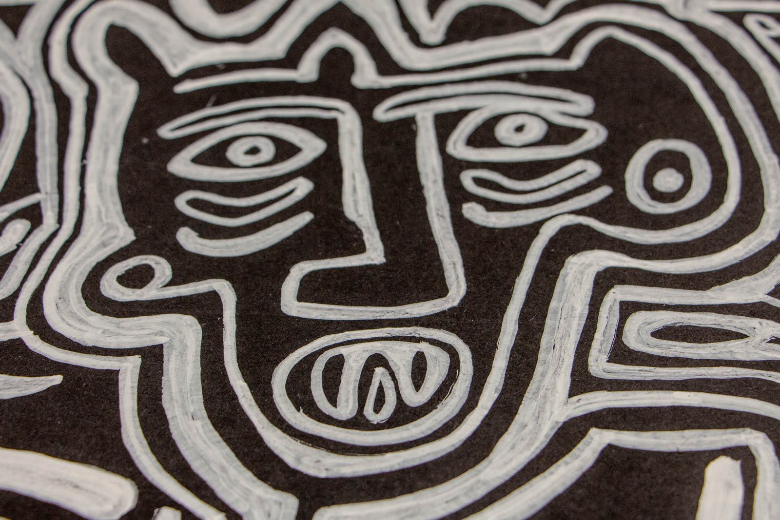 Metamorphic Entwining 003 detail: compact, feline-eared figure with almond eyes and oval mouth showing seed-like marks; white ink on black paper