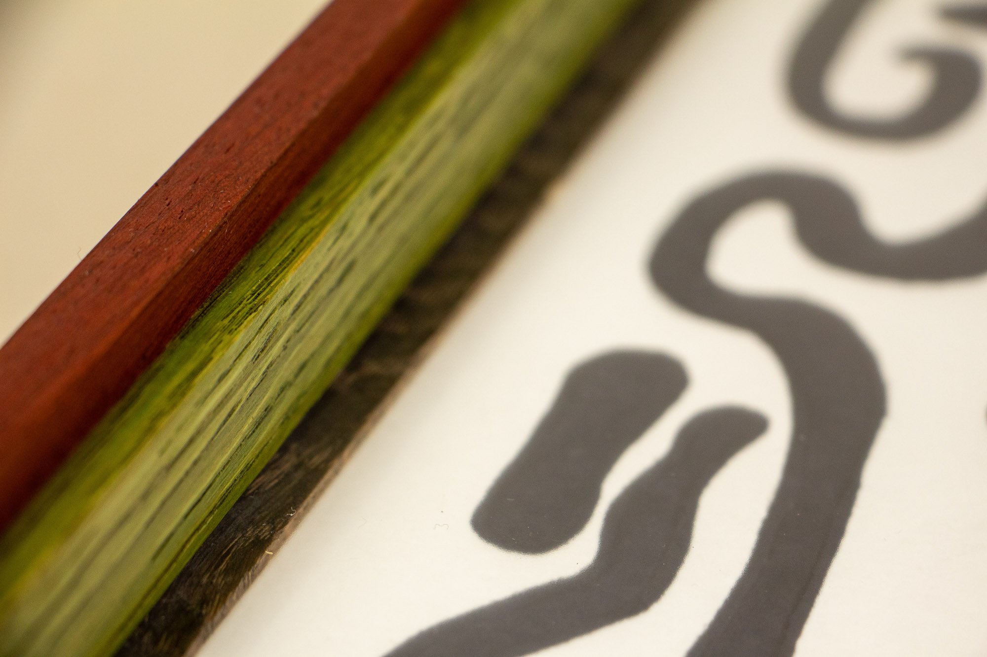 Resonant Syntax 003 frame: horizontal close-up of the frame profile, showing a layered red, green, and granada sequence with distinct grain variation and a refined satin finish across the mahogany-and-oak construction