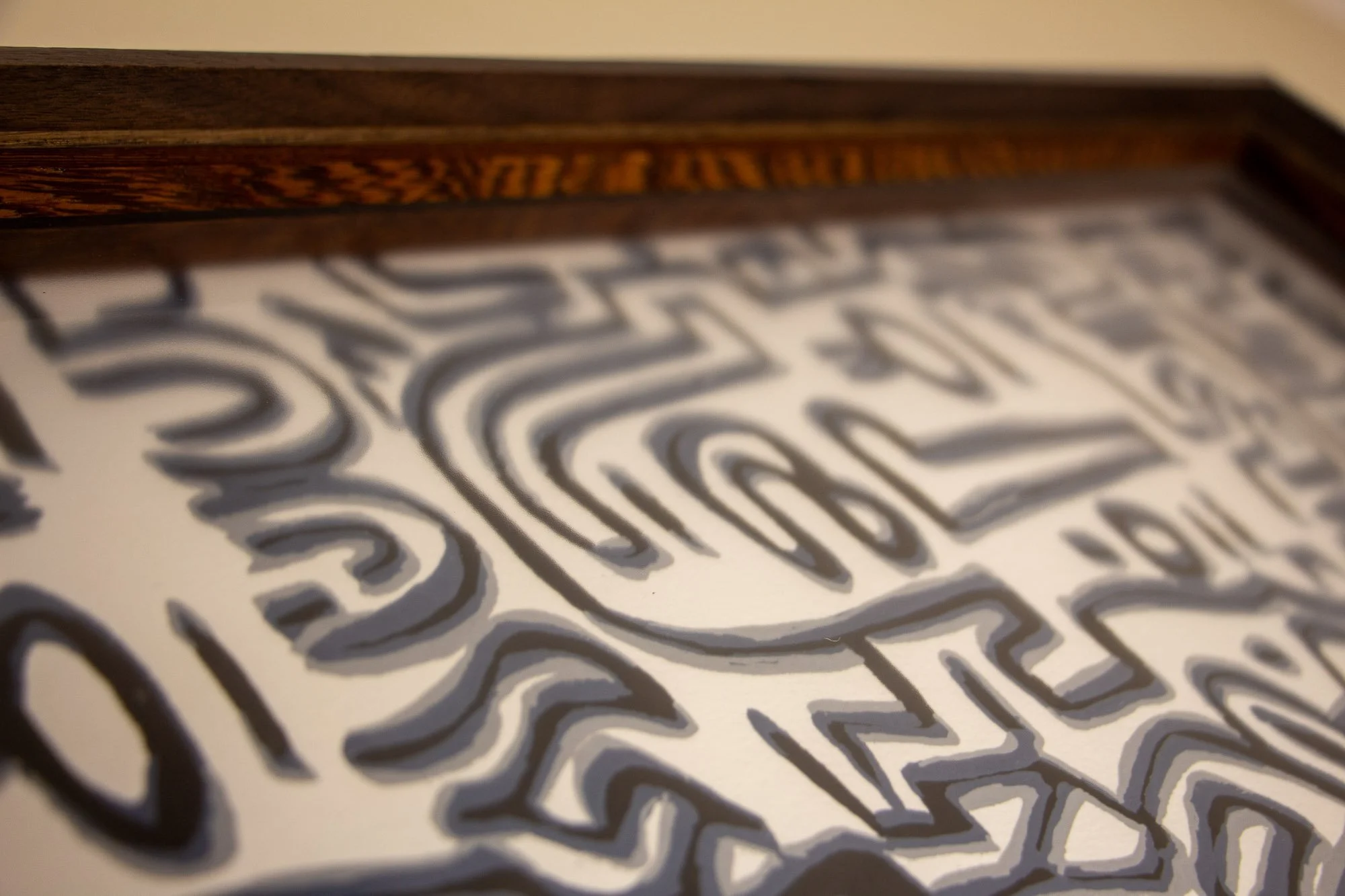 Luminous Parallax 004 frame: low-angle detail across the glazing and upper frame edge, drawing attention to the frame’s inner banding and the layered spatial depth between glass, artwork, and wood.