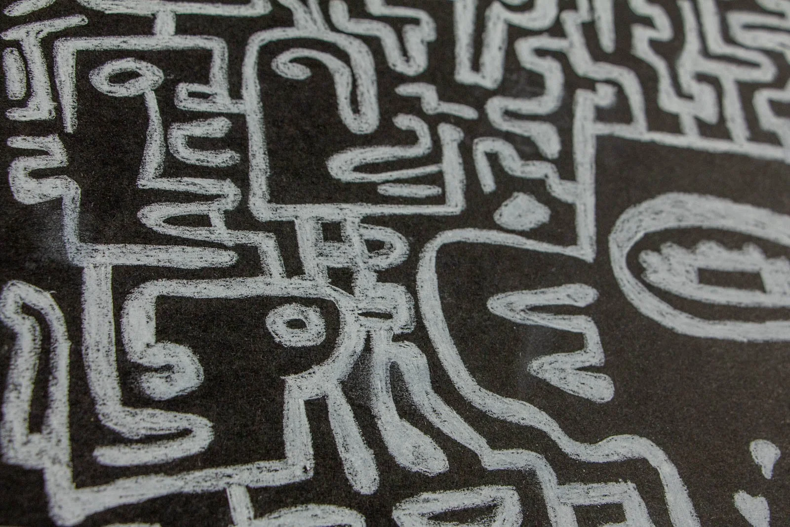 Synaptic Mythos 001 detail: profile cluster, tiny faces and curls pressed to the border; turning lines show pressure shifts; chalk-white on deep charcoal stock