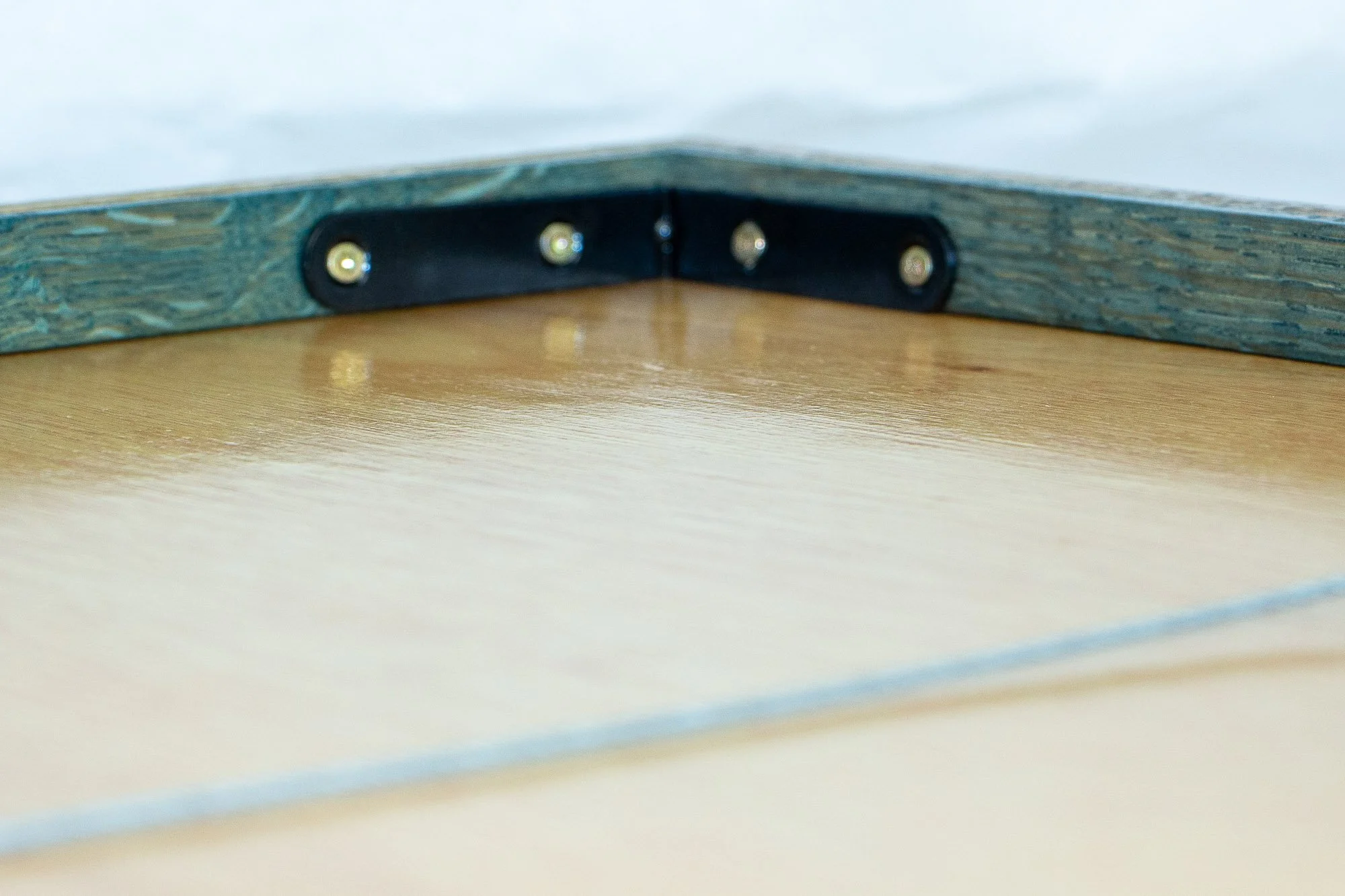 Elusive Cocoon 002 frame: rear corner detail with a black metal corner brace, brass screws, pale wooden backing board, and a green-toned inner frame edge.