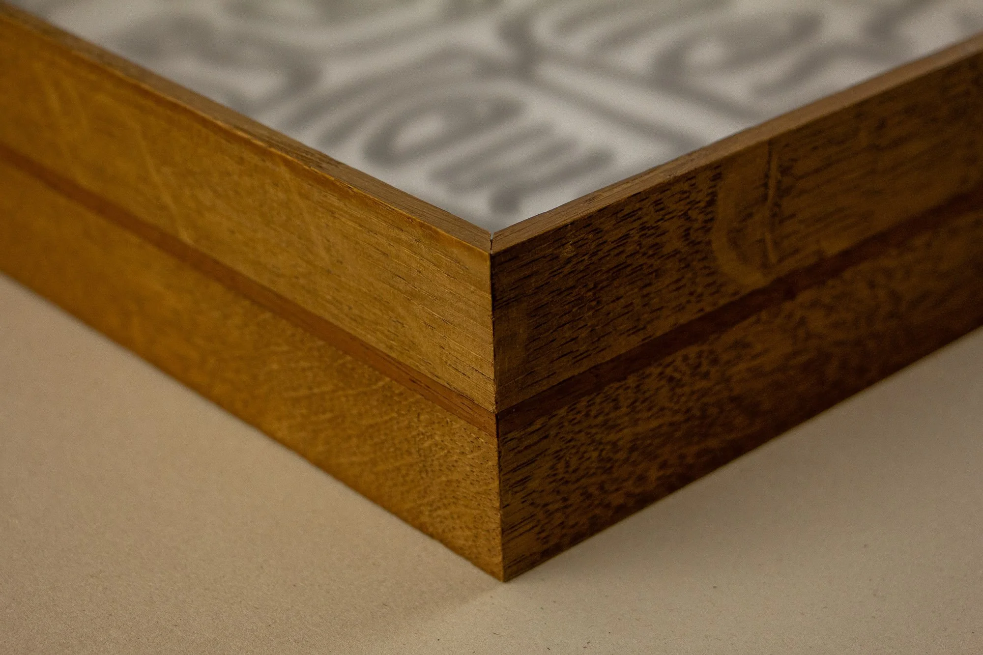 Veiled Alchemist 004 frame detail: close-up of the front corner, showing the meeting of the mitred edges, the reddish inner band, and the softly receding artwork visible beneath the glazing.