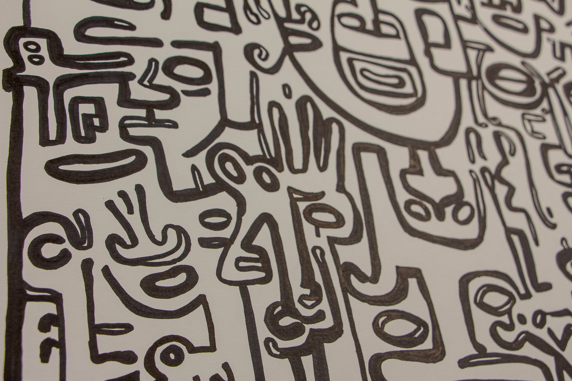 Veiled Alchemist 002 detail: angled close-up of interlocking black line faces and symbols on white paper, showing a layered composition of profiles, eyes, and abstract forms held in a dense visual rhythm.