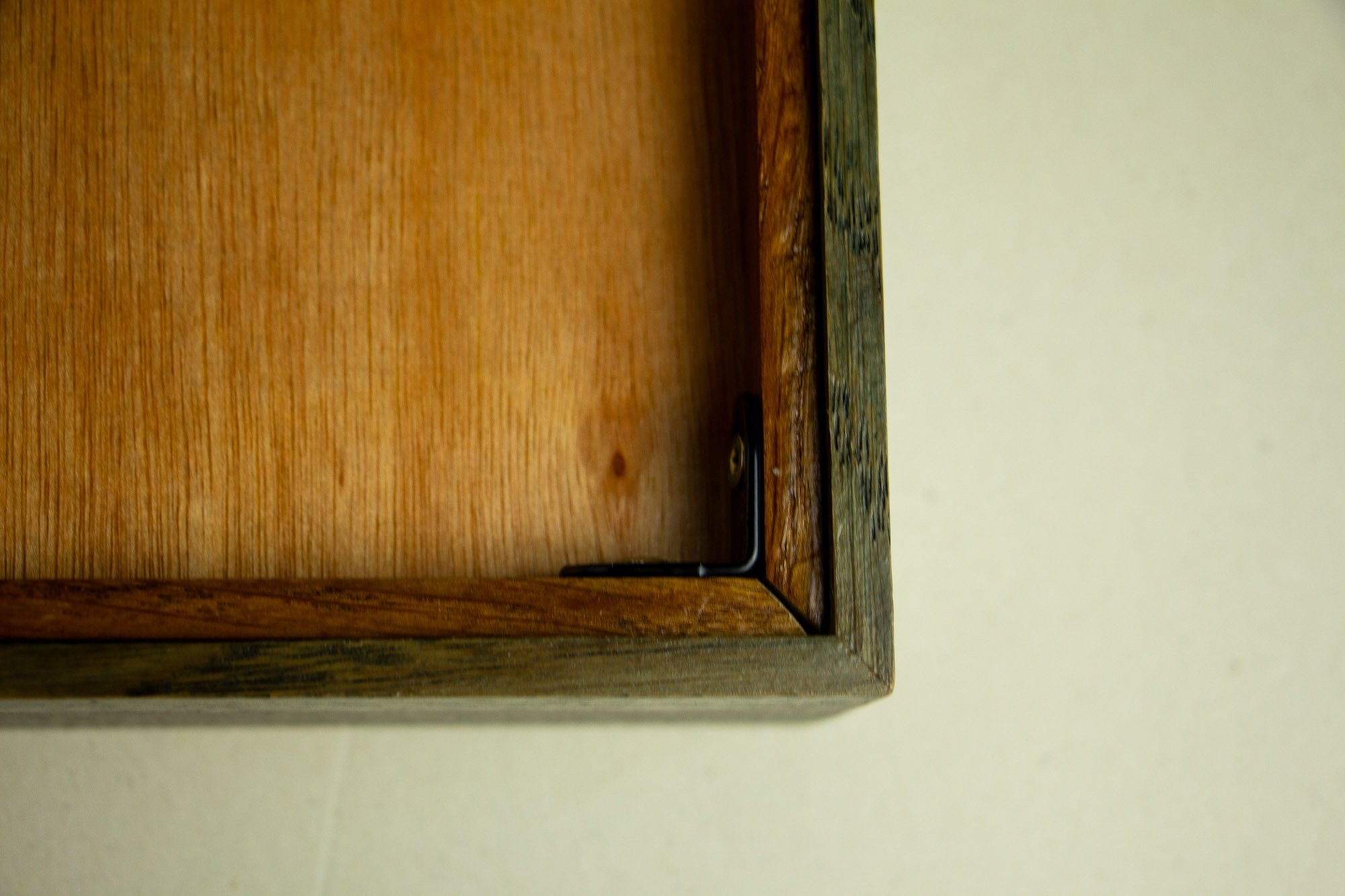 Eclipsing Gravitas 002 frame verso: back corner detail showing the mitered construction, inner backing rim, warm meranti plywood panel, and a black metal corner bracket securing the frame from the reverse.