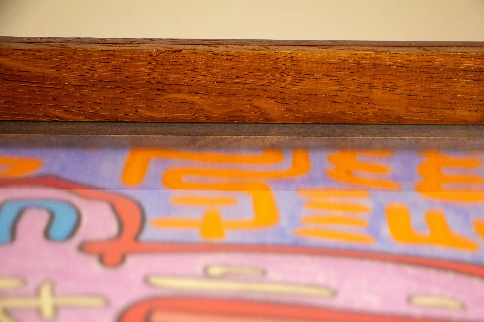 Unseen Signifiers 010 frame detail: low horizontal close-up of the upper frame edge, with the warm wood grain and lacquered finish sharply in focus above the softly blurred artwork behind the acrylic. mahogany, oak and beech wood.