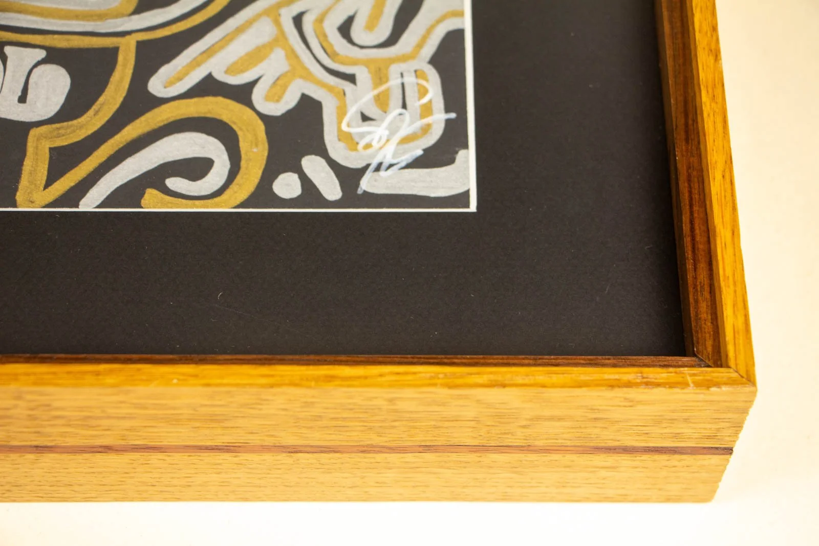 Golden Nostalgia 001 frame: lower-right corner, artist signature set against a deep black window mat; slim white paper reveal; outer oak rail shows the centered mahogany pinstripe