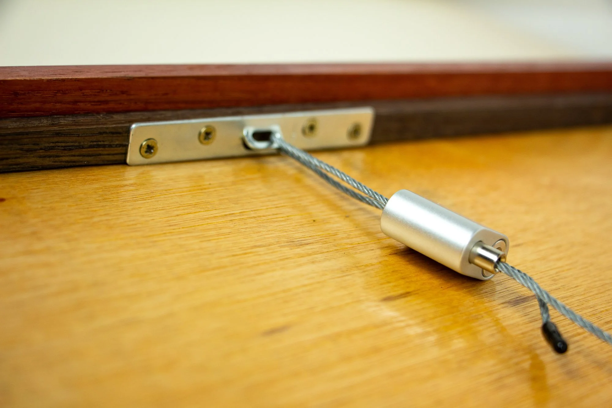 Resonant Syntax 003 frame: reverse detail of the hanging system, with steel cable, silver locking mechanism, metal mounting plate, meranti plywood back panel, and the layered frame construction in red and granada tones