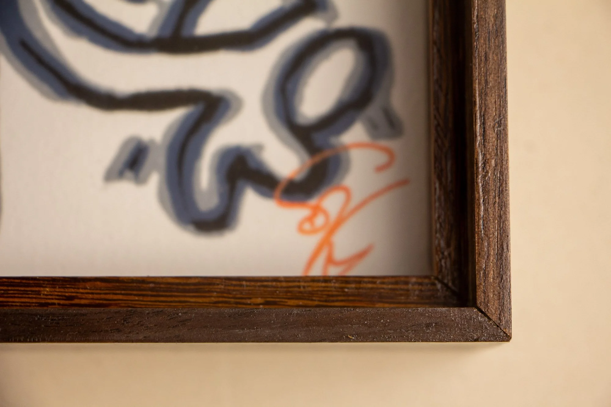 Luminous Parallax 003 frame: lower corner detail with the artist’s orange signature visible behind glass, framed by the dark outer edge and the warm-toned inner structure.