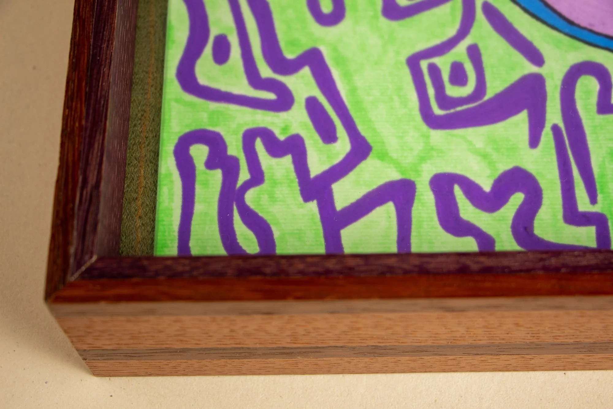 Unseen Signifiers 005 frame detail: lower-left corner of the framed work, showing the reddish-brown outer frame, olive-green inner reveal, and the artwork’s lime-green field with purple symbols visible behind the glazing. mahogany, oak and beech wood