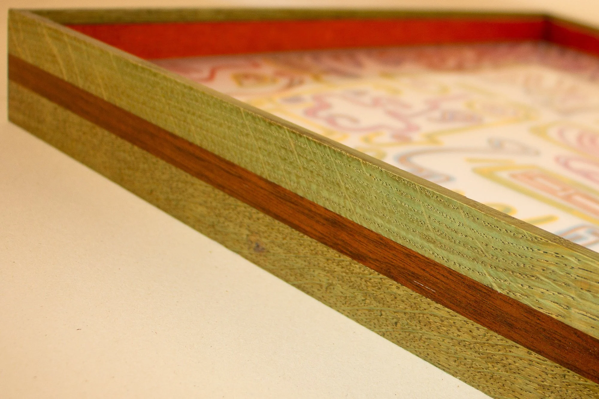 Eclipsing Gravitas 001 frame: angled front-side detail of the layered oak-and-mahogany frame, combining green-toned oak with a warm mahogany band in a low-profile construction around the artwork.