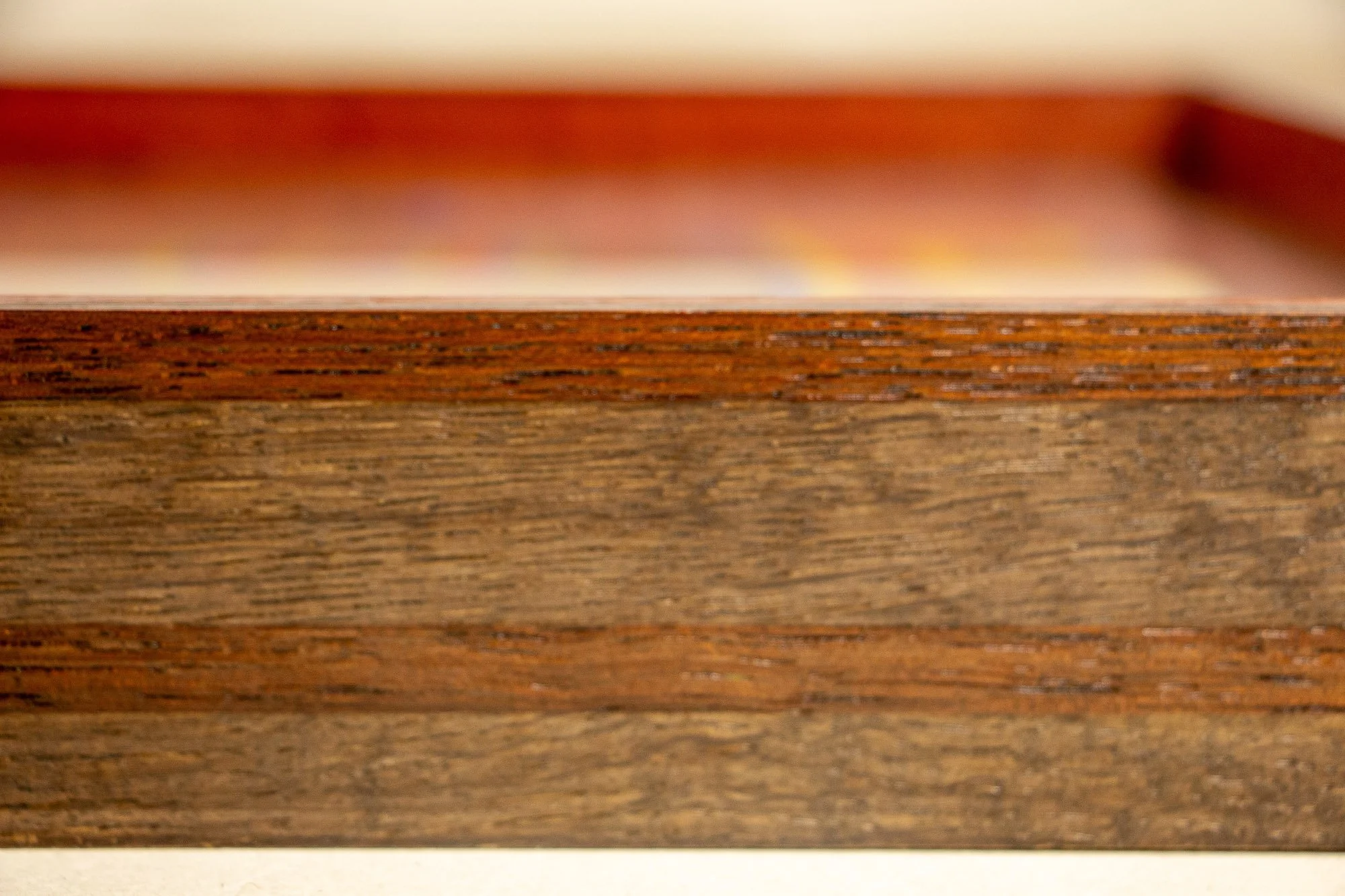 Unseen Signifiers 003 frame detail: shallow-focus side view of the frame, where the stacked wood layers appear in soft bands of reddish brown and smoky taupe beneath the glass edge. mahogany, oak and beech wood.