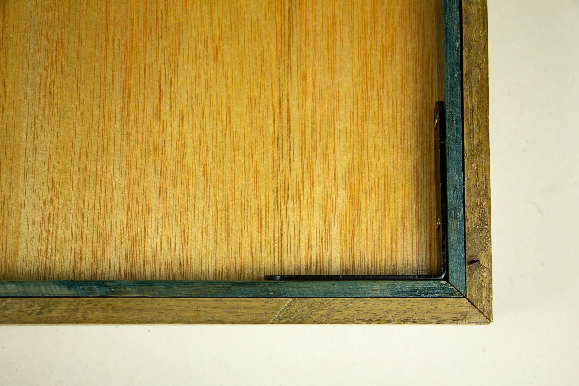 Elusive Cocoon 002 frame: overhead reverse-side corner detail showing the mitered outer frame, green-toned inner liner, wooden backing board, and black metal corner brace.