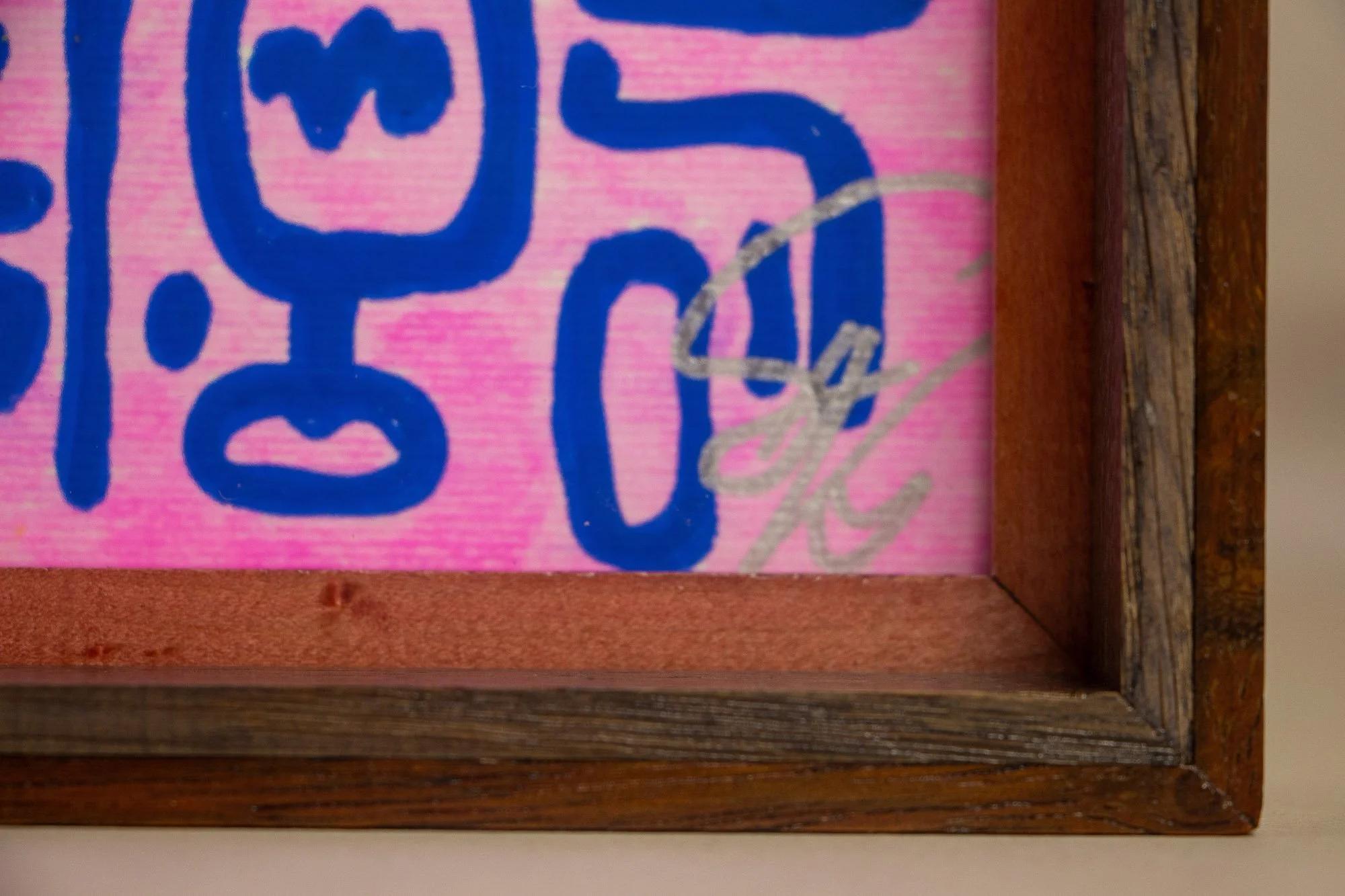 Unseen Signifiers 007 frame detail: close-up of the lower-right corner of the framed artwork, showing the silver signature on the pink ground and the layered wooden frame meeting at the miter. mahogany, oak and beech wood.