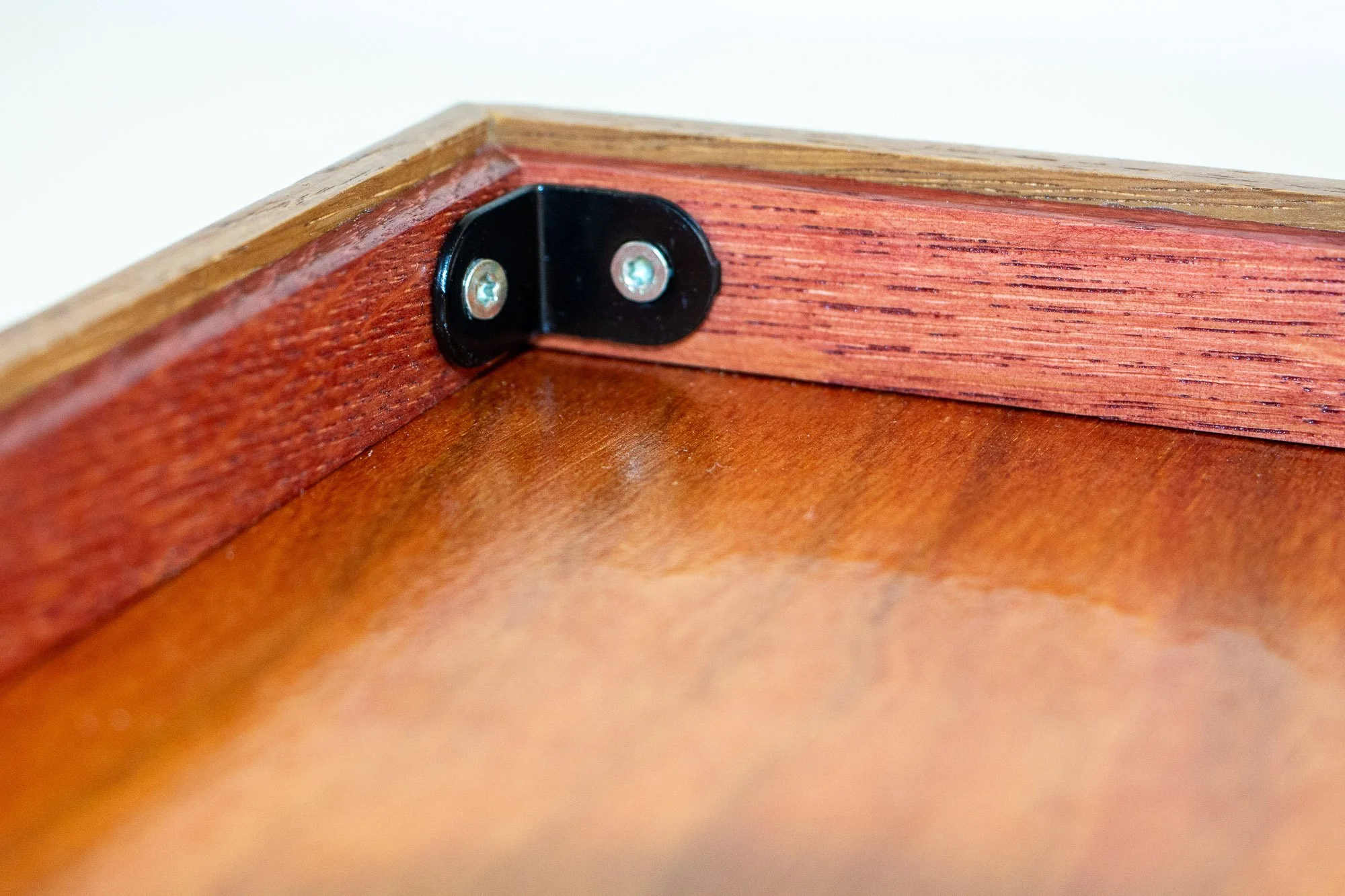 Veiled Alchemist 002 frame detail: close-up of the rear inside corner, highlighting the black corner bracket, reddish inner rear rim, and the polished finish of the back panel and structural joinery.