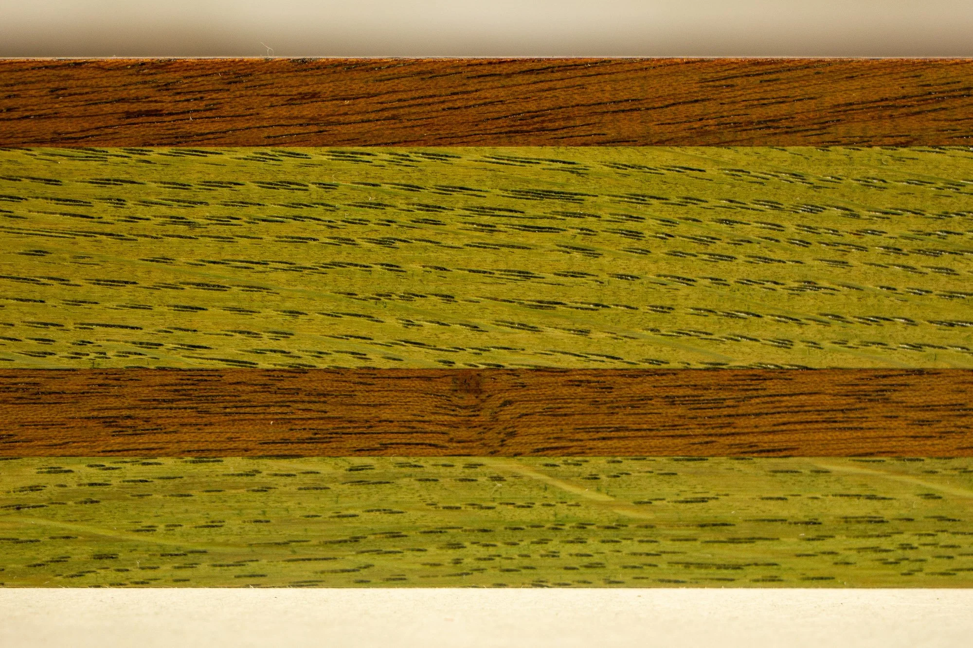 Resonant Syntax 004 frame: frontal close-up of the frame profile, showing layered green and granada-red bands with visible oak grain, tonal variation, and a clean satin finish across the wood surface