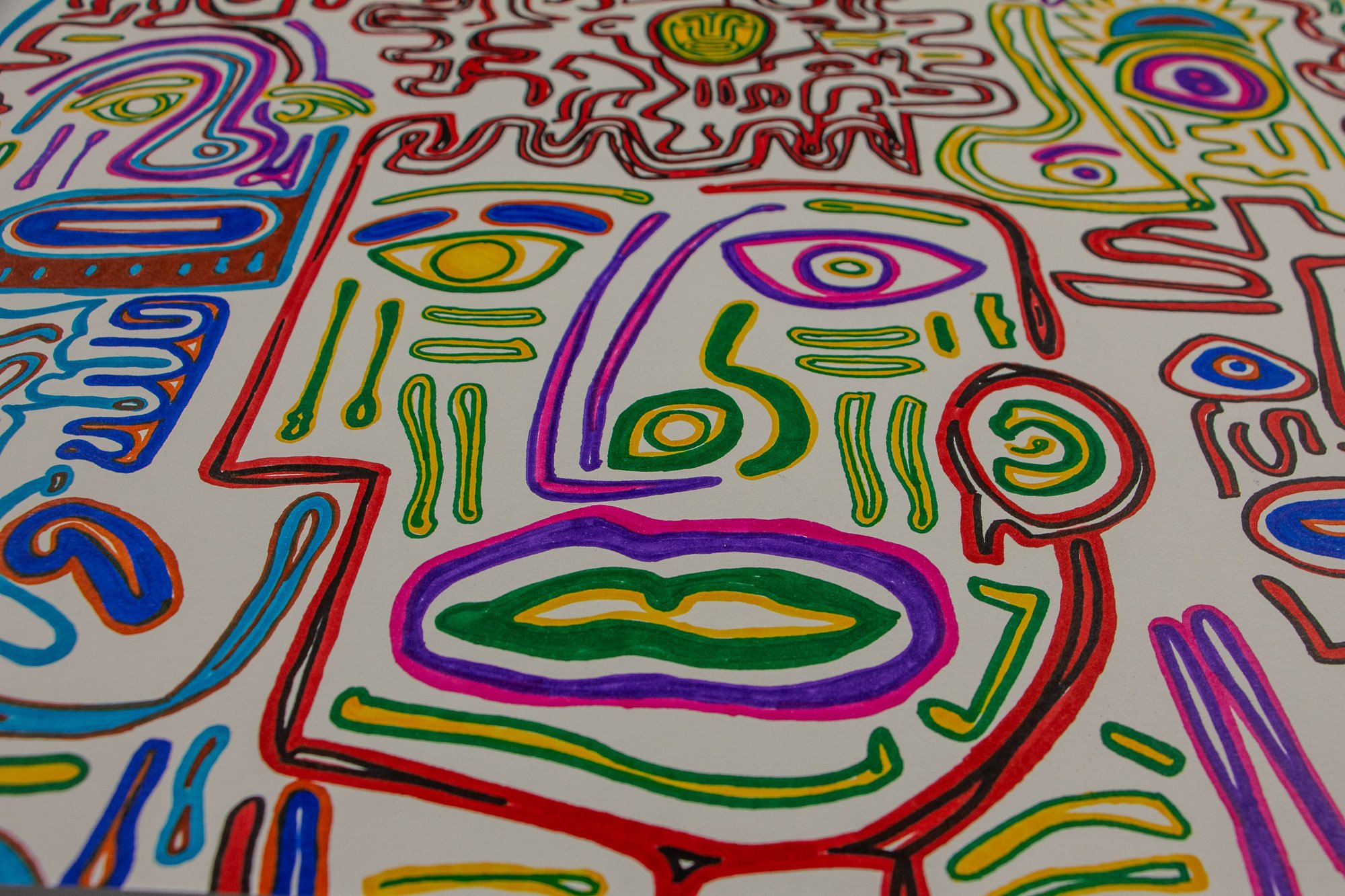 Eclipsing Gravitas 002 detail: close-up of a central multicolored face-like form with asymmetrical eyes, green and yellow mouth, purple and pink contours, and red spiral accents on white paper.