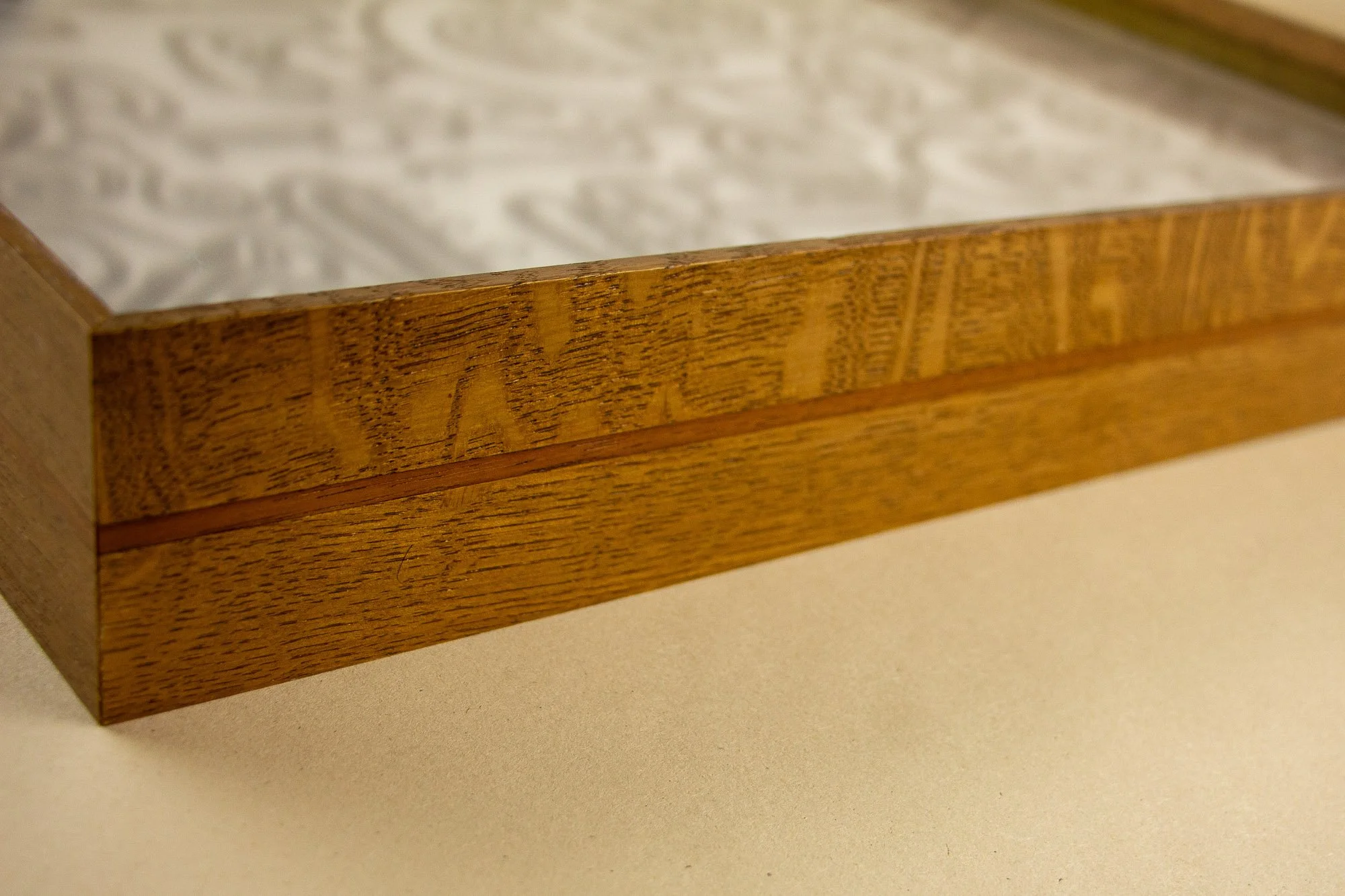 Close-up of a wooden art frame with a light-colored textured surface, showing the wood grain and a horizontal decorative strip.