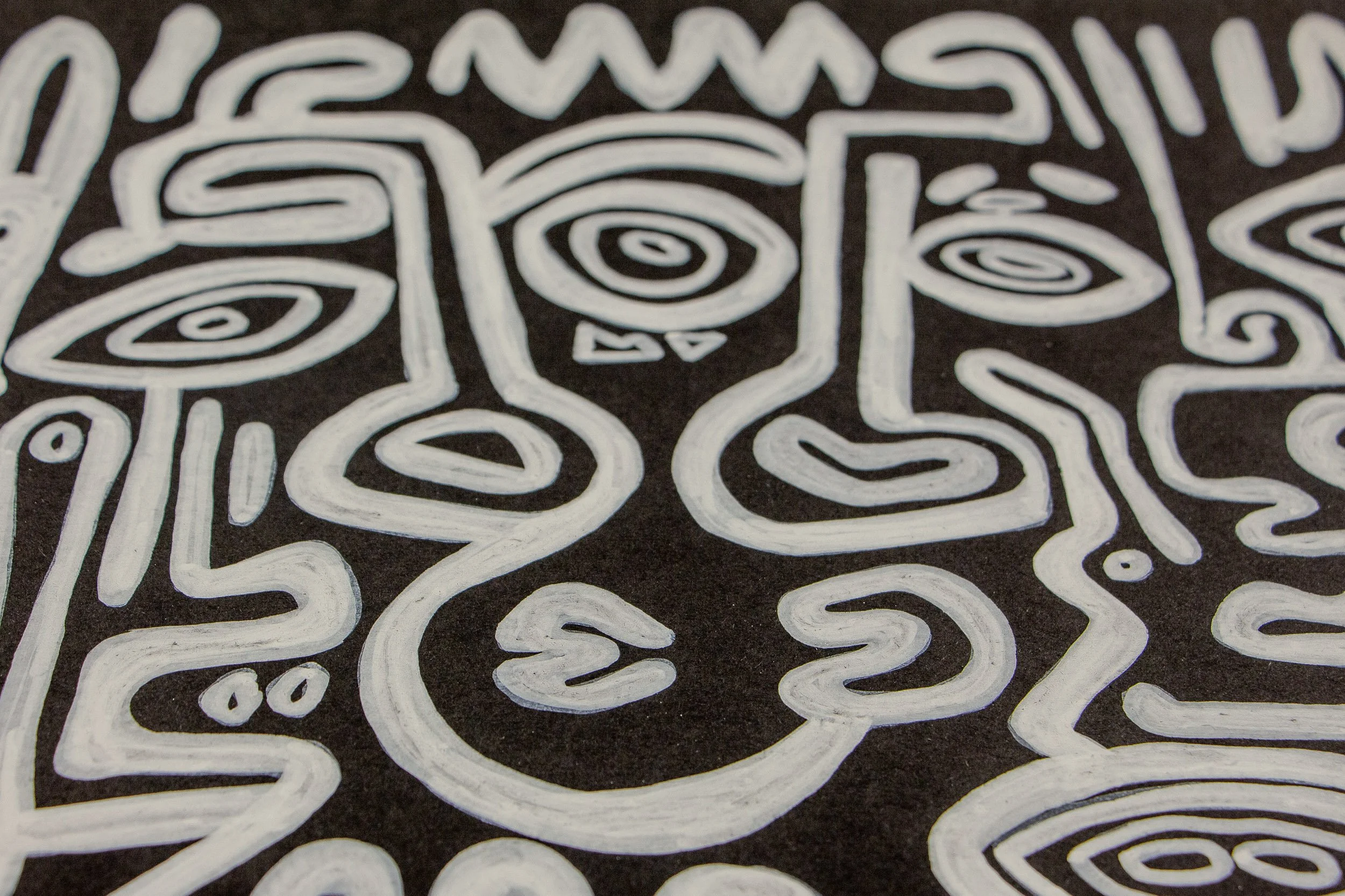 Turbulent Aegis 003 detail: close-up of clustered face-like forms and eye symbols, revealing the dense network of white lines, varied expressions, and the grain of the wooden surface beneath the paint.