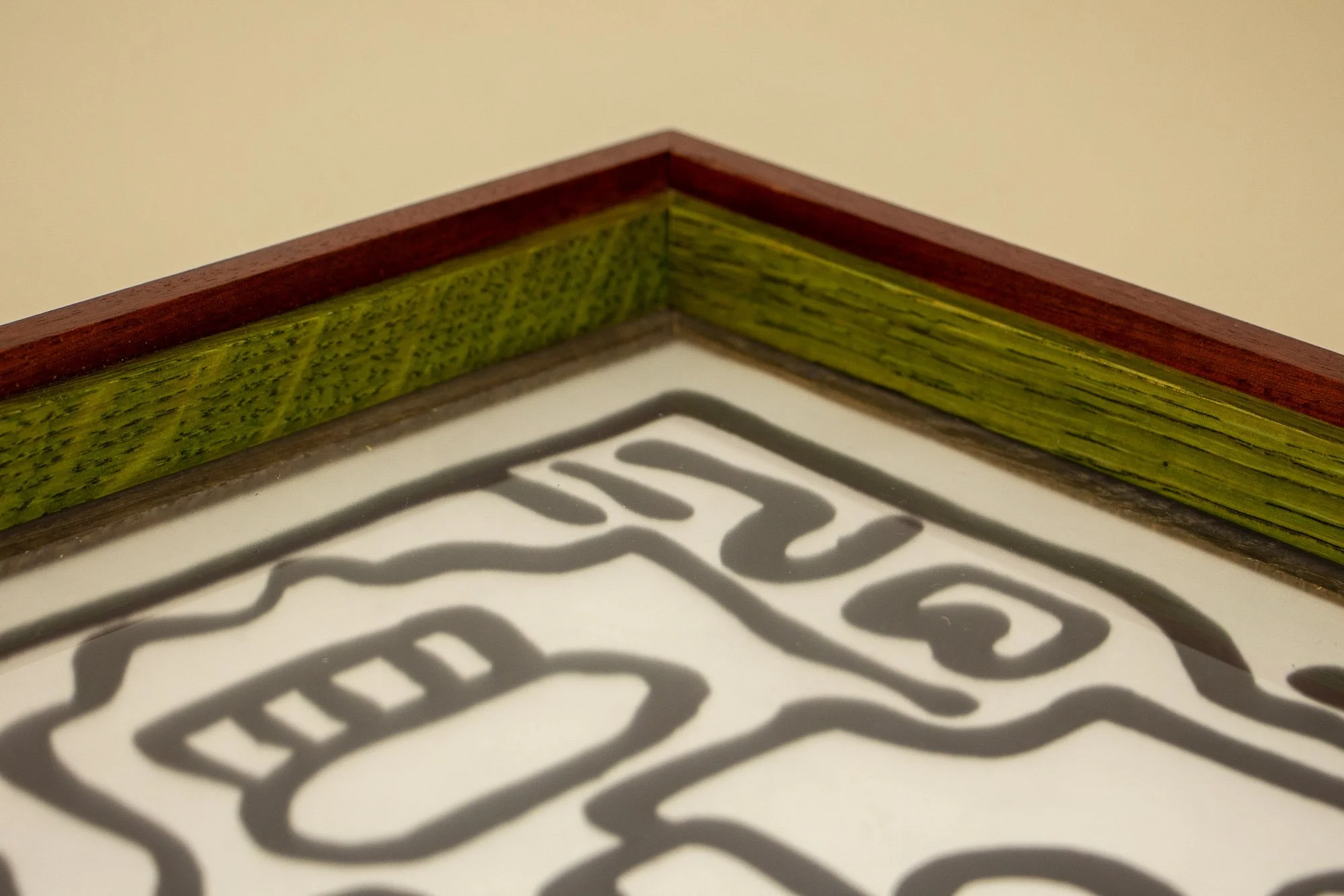 Resonant Syntax 003 frame: angled close-up of the frame edge, with red outer band, vivid green inner layer, dark granada lip, and the artwork surface visible beneath the glass