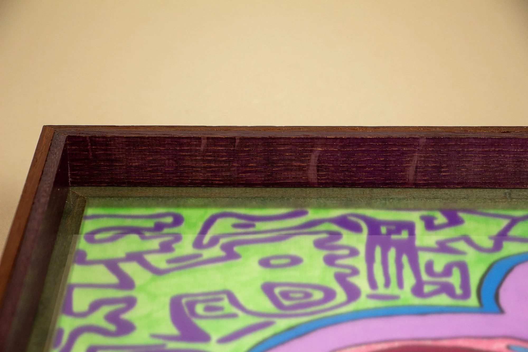 Unseen Signifiers 005 frame detail: upper edge close-up of the framed work, showing the deep reddish-brown top rail, muted olive-green inner reveal, and the lime-green and purple artwork receding beneath the glazing. mahogany, oak and beech wood.