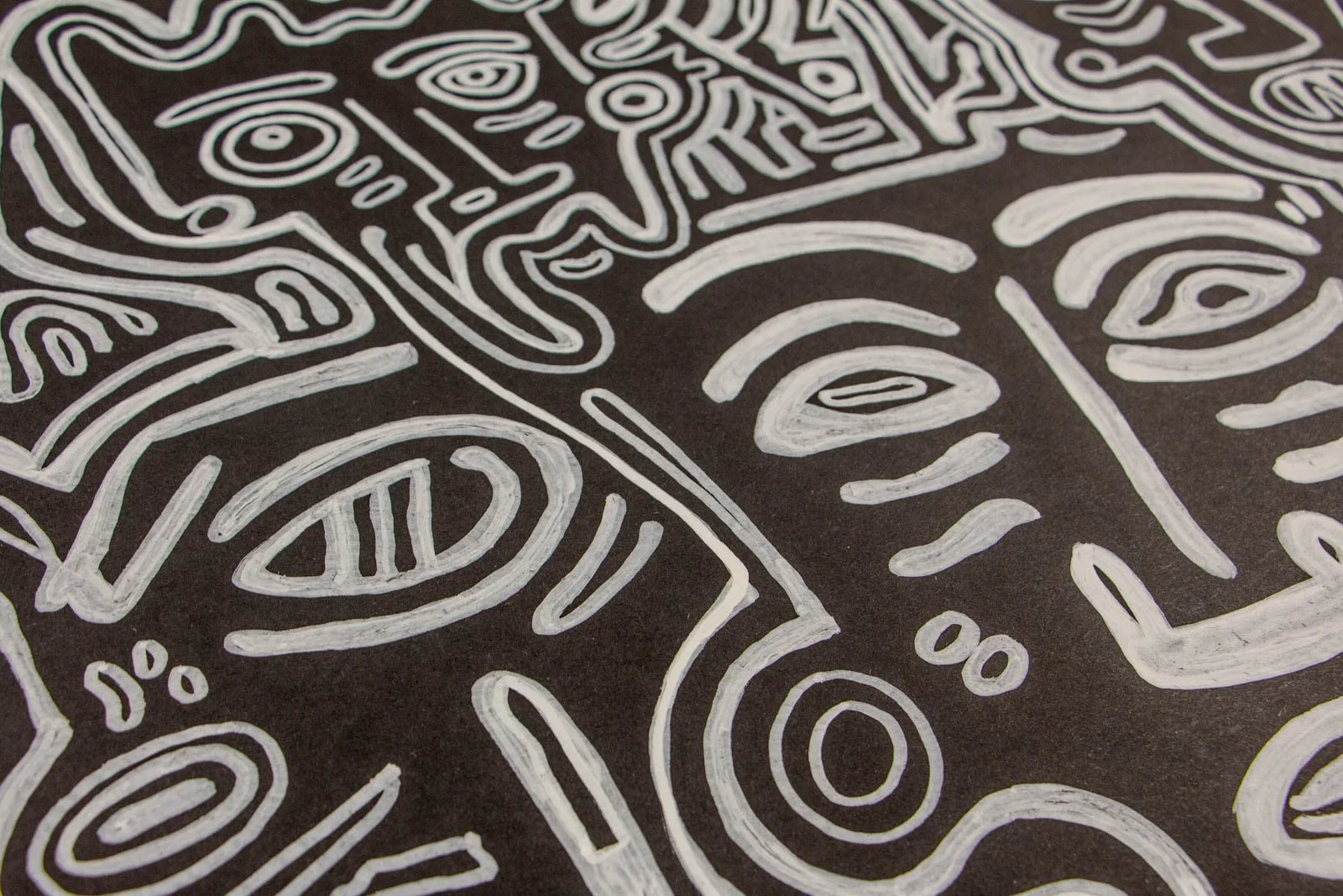 Metamorphic Entwining 003 detail: overlapping faces with heavy lids, cheek dashes, and a circular cheek/ear motif; white ink on black paper