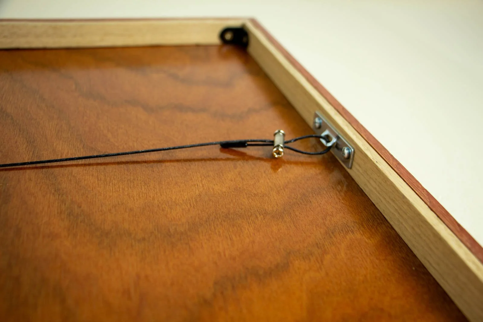 Silence’s Caesura 003 frame: hanging wire sweep, black-coated cable drawn taut to the anchor; glossy backboard throws a soft reflection