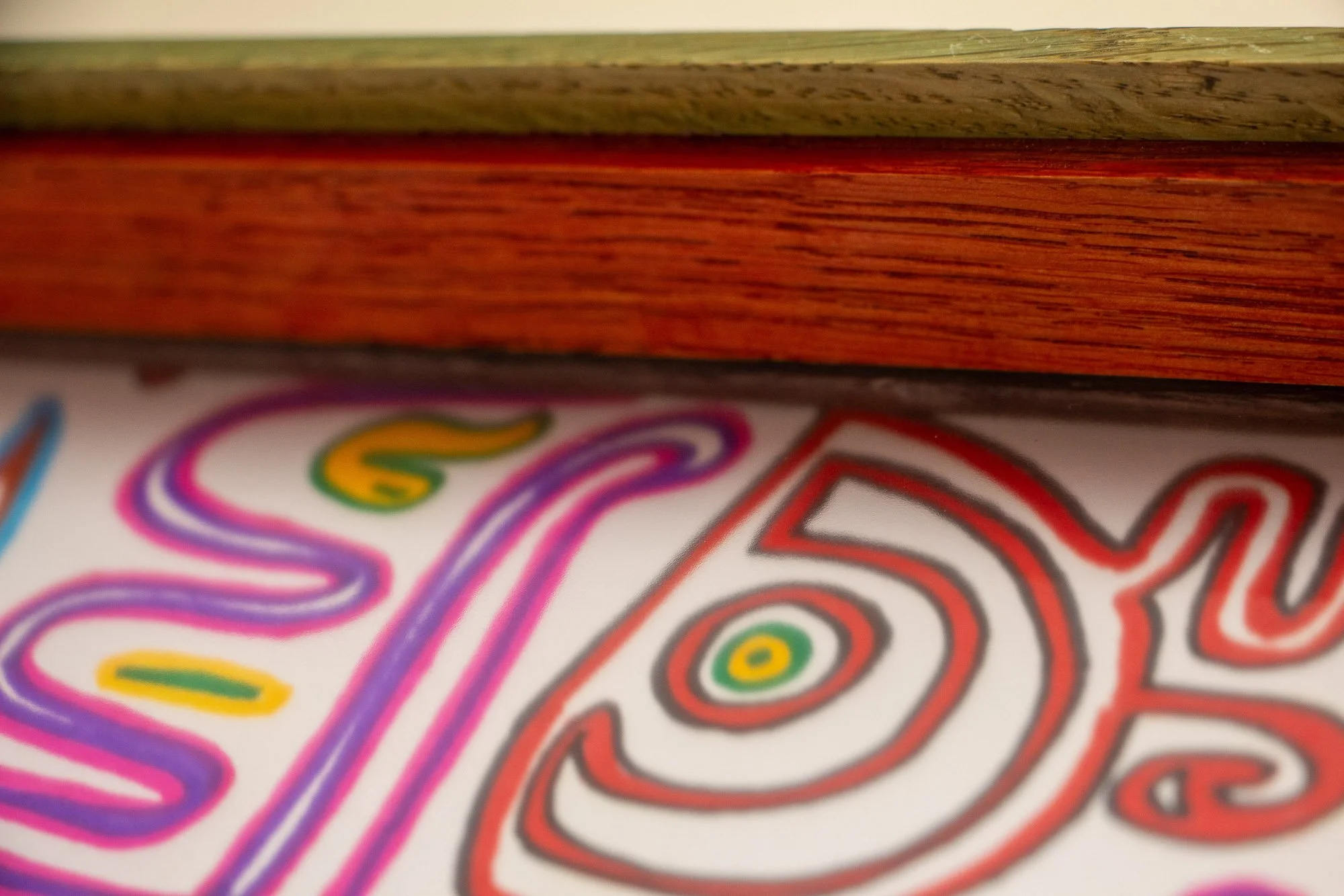 Eclipsing Gravitas 001 frame and signature: signed lower corner with blue signature on white paper, set inside a layered oak-and-mahogany frame with a red inner lip, green-toned oak band, and warm mahogany edge.