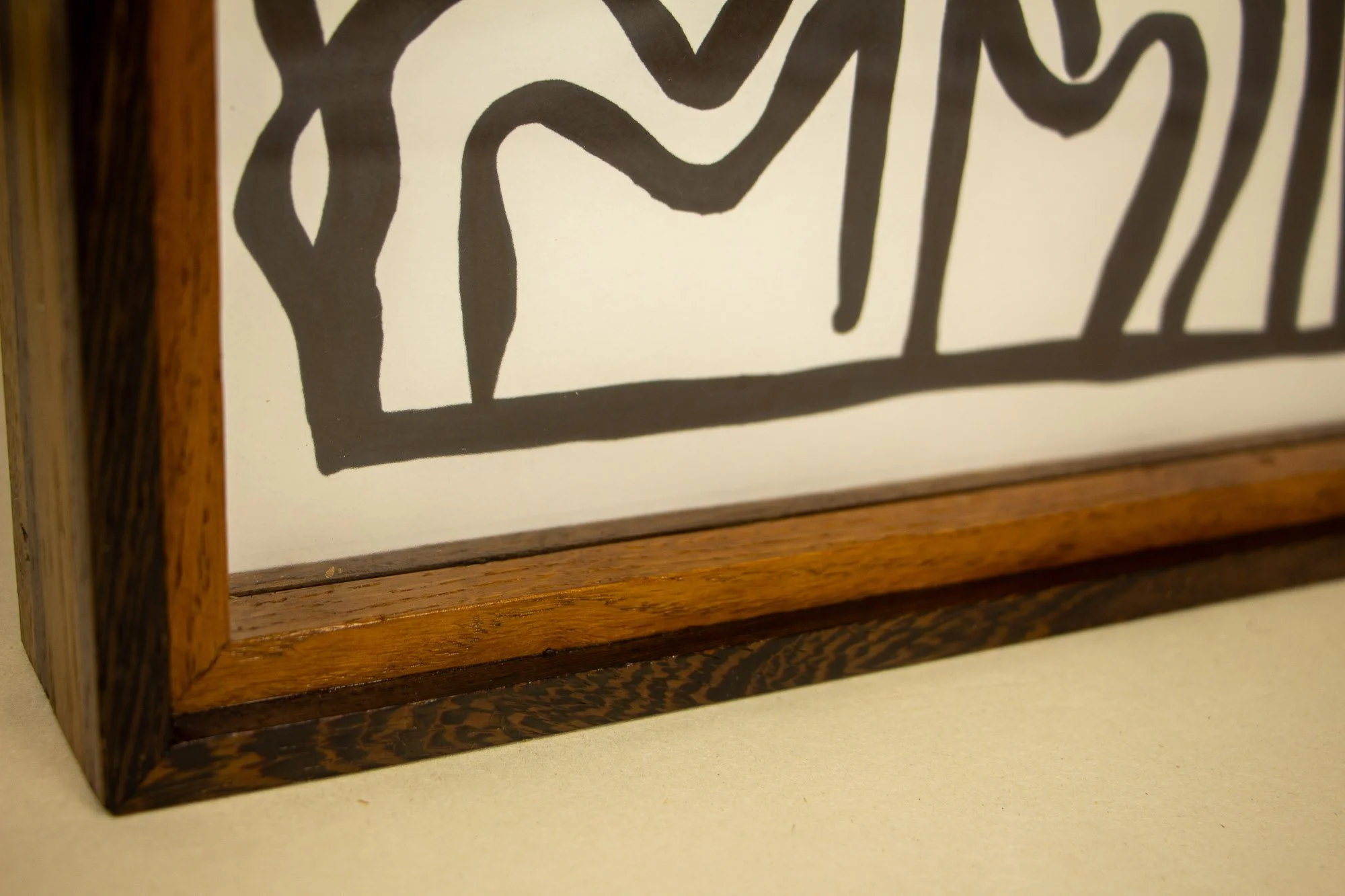 Elusive Cocoon 002 frame: low frontal view of the frame edge with a dark top rail, broad golden oak-toned face, and darker figured strip beneath the glass-covered artwork.