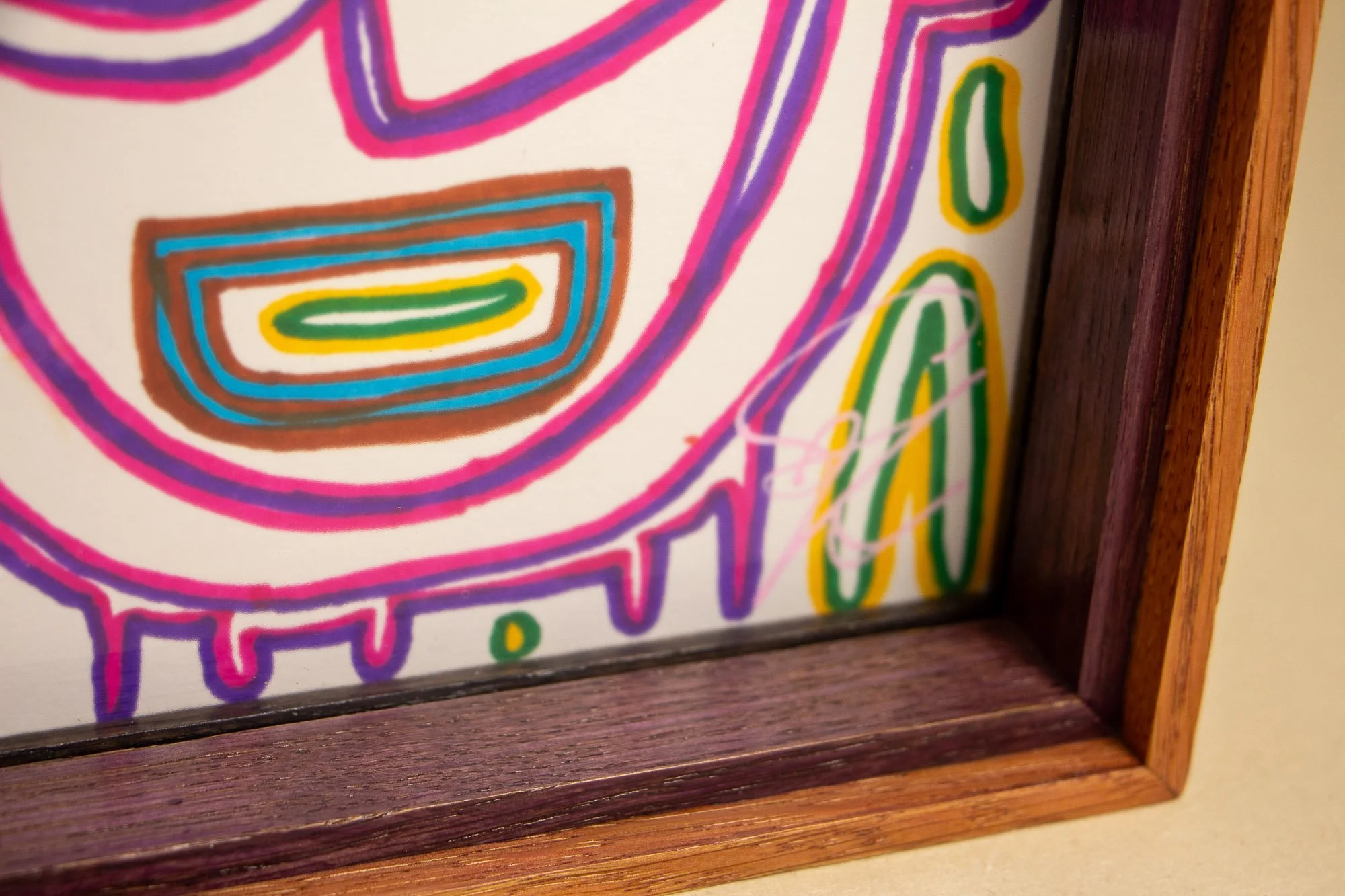 Eclipsing Gravitas 003 frame: close corner detail with the pink signature visible near the glass edge, framed by the dark purple inner lip and the warm pink-orange outer frame in a tight, sharply focused composition.