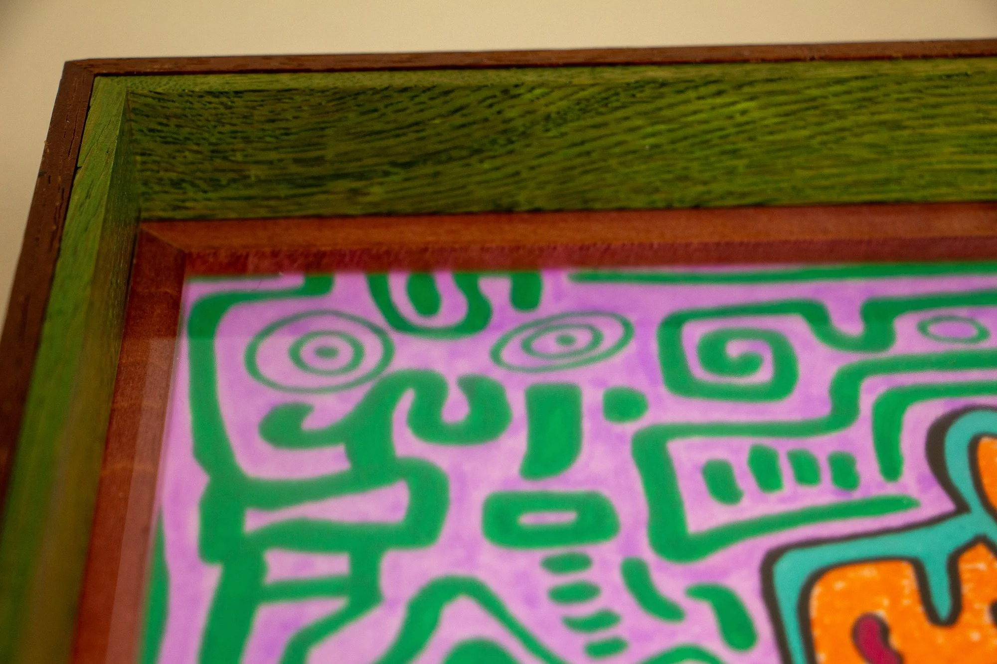 Unseen Signifiers 002 frame detail: upper-left corner view of the frame, showing the green inner band, reddish inner spacer, and the lilac artwork field with green symbols beneath the glass. mahogany, oak and beech wood.