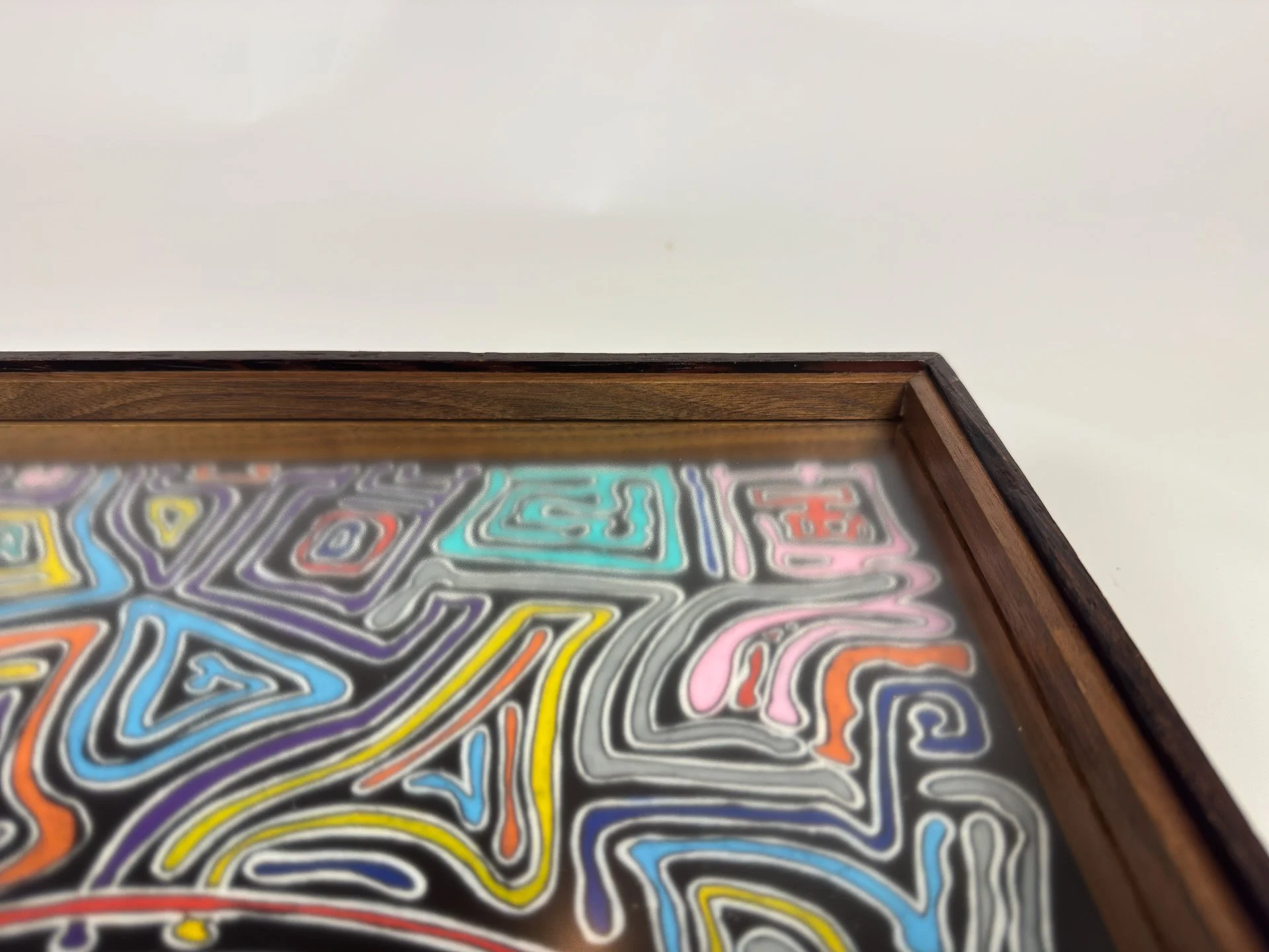 Detail of the upper frame section with the artwork beneath, showing the contrast between deep wood tones and vivid colored line work, as the frame holds the composition in a carefully built order.