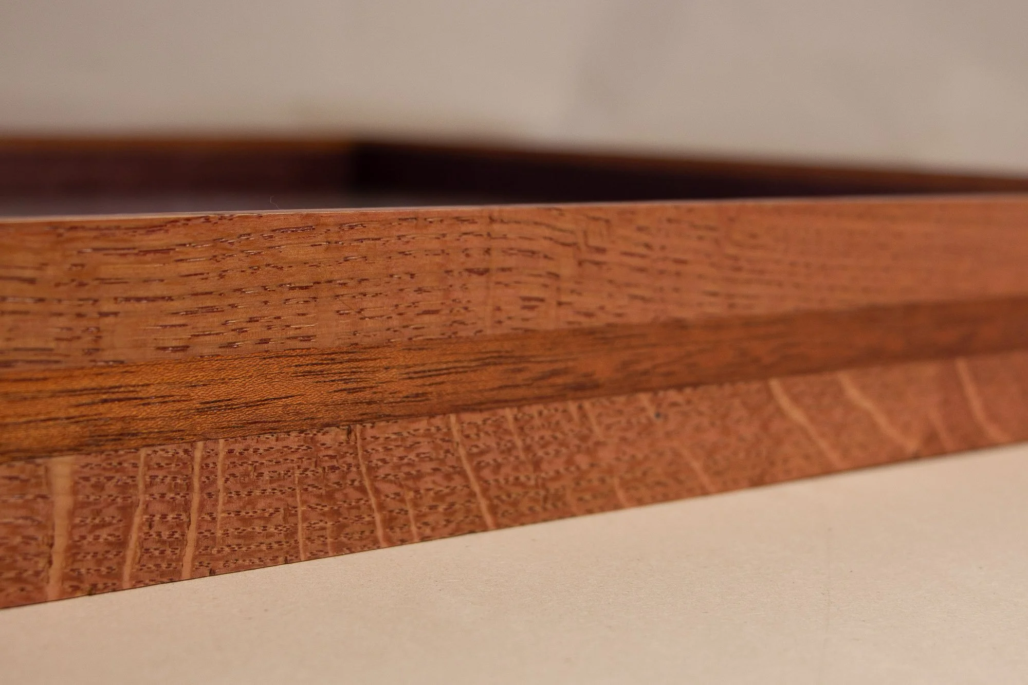 Eclipsing Gravitas 003 frame: close side detail of the layered frame, emphasizing the contrast between the warm pink-orange toned oak and the darker mahogany strip, with the top edge tapering cleanly toward the glass.