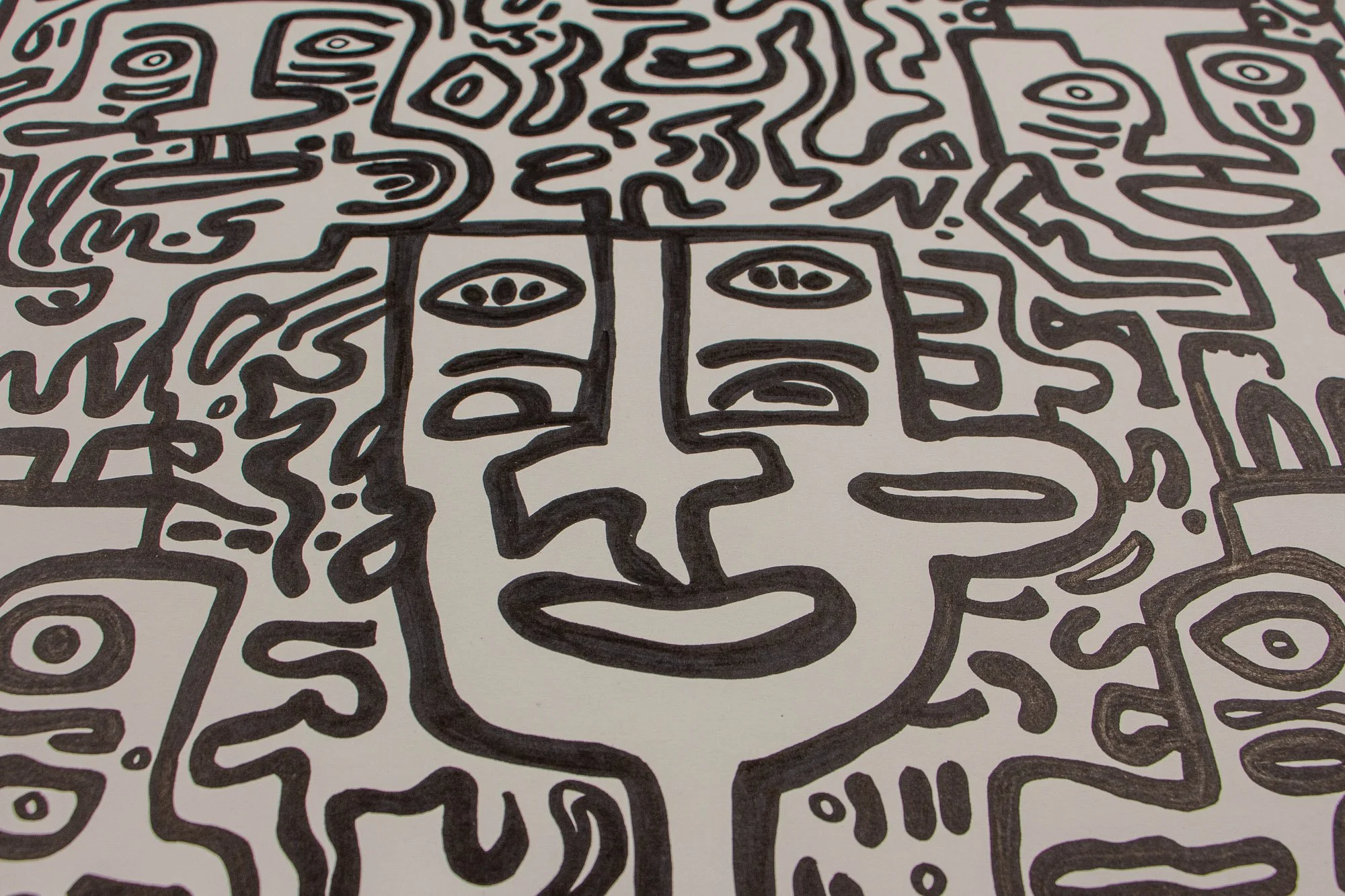 Veiled Alchemist 003 detail: close-up of a central frontal face with asymmetrical eyes, a long nose, and a rounded mouth, surrounded by tightly interwoven abstract figures and flowing black contours on white paper.