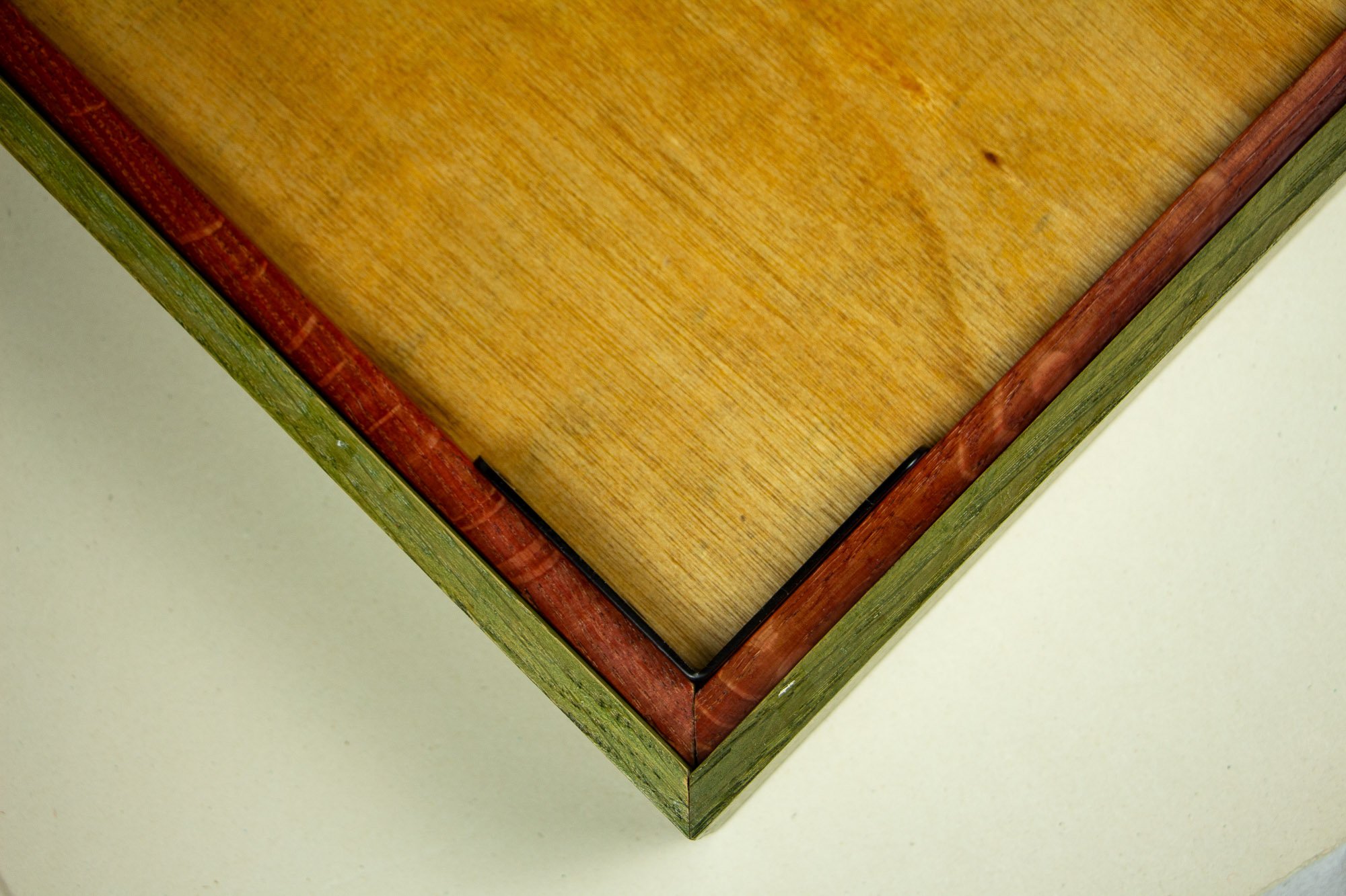 Resonant Syntax 004 frame: reverse corner detail of the frame construction, showing the meranti plywood back panel, black metal corner bracket, red inner rim, and green outer frame edge