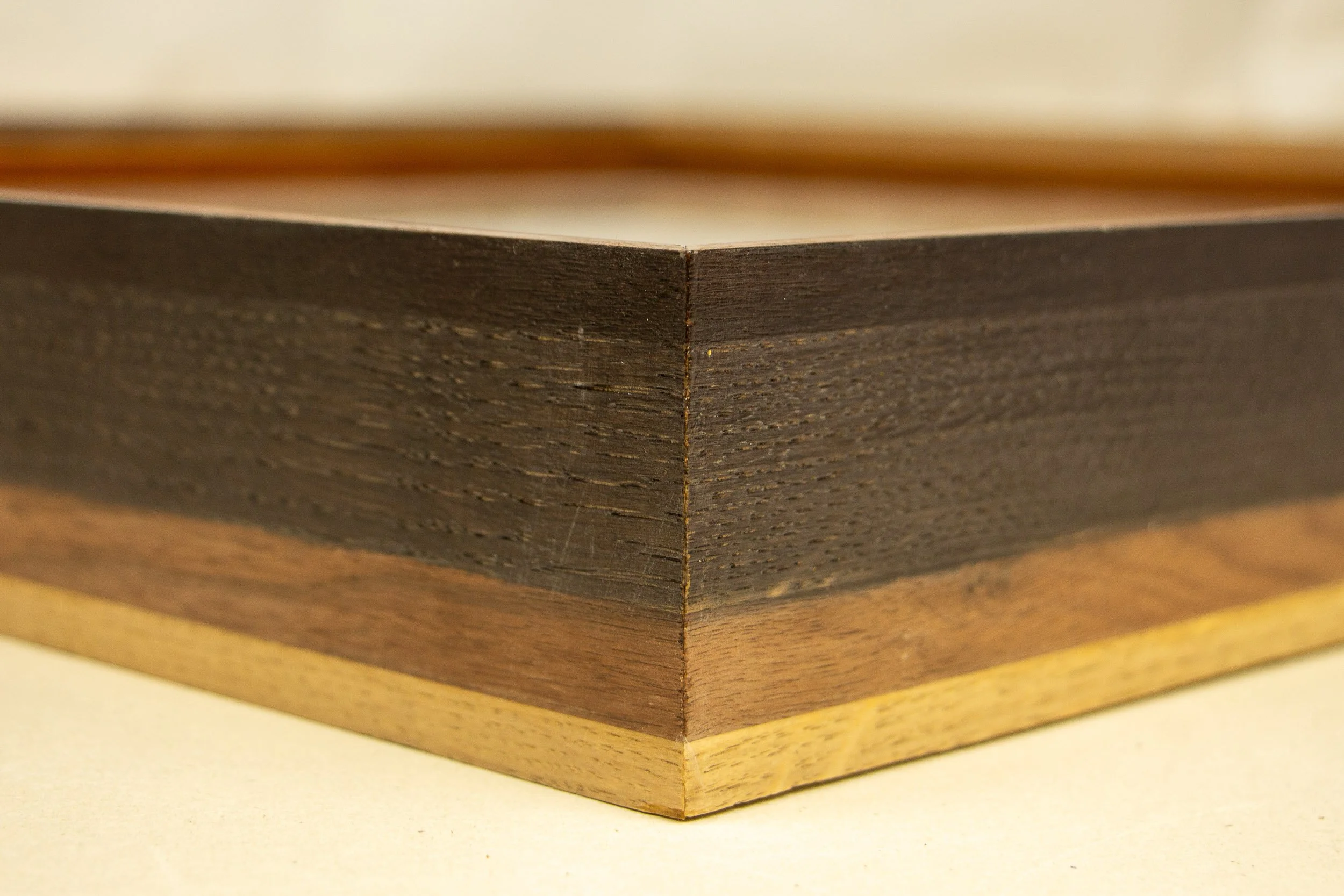 Mêlée of Discovery 004 frame: corner detail of the exterior profile, showing the layered construction in dark walnut, warmer mid-tone walnut, and light oak.